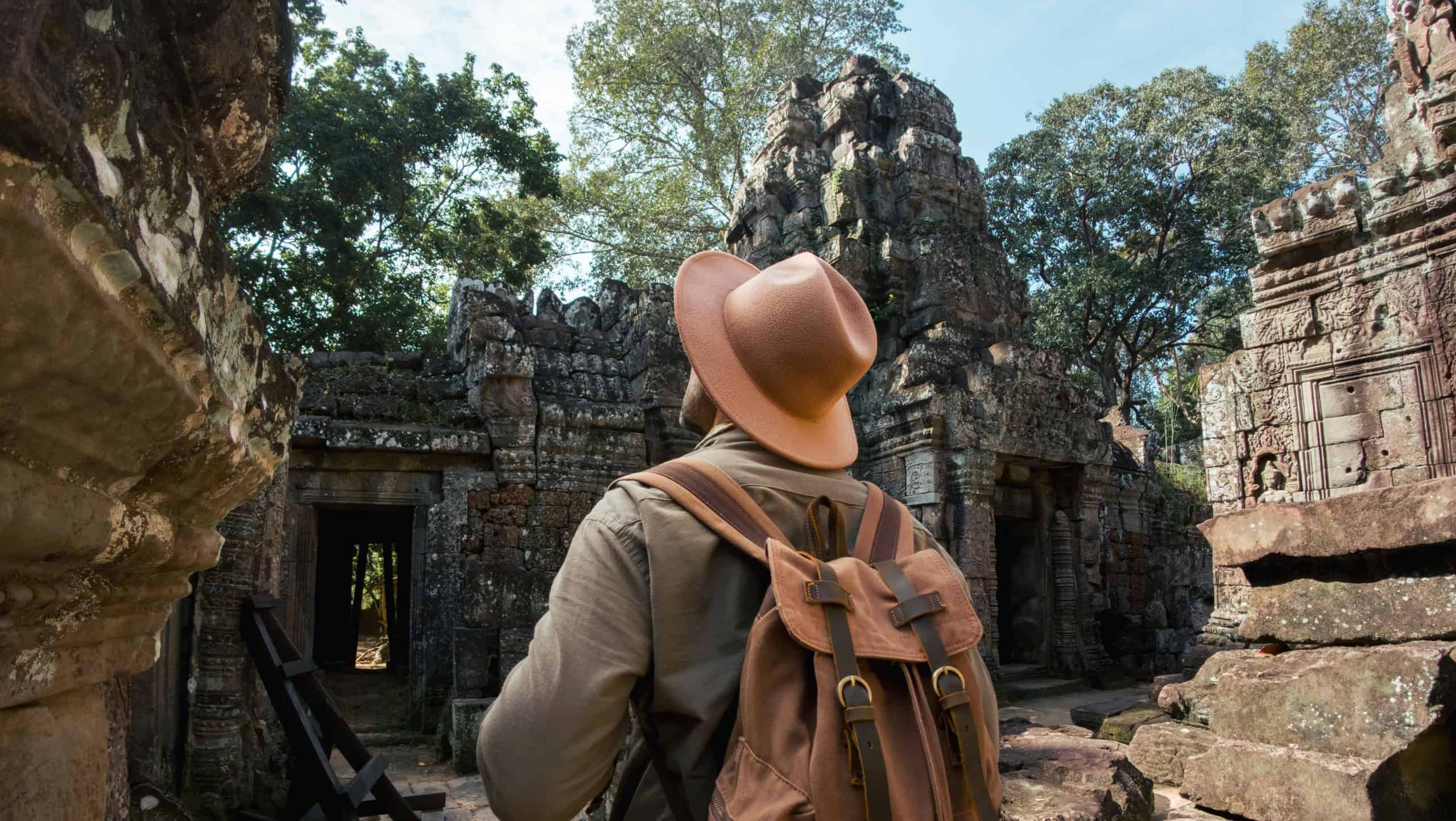 Male traveler with a backpack and hat walks into the ancient ruins of Ta Som temple in Angkor Wat, Cambodia. Perfect stock image for travel blogs, adventure content, or tourism ads.