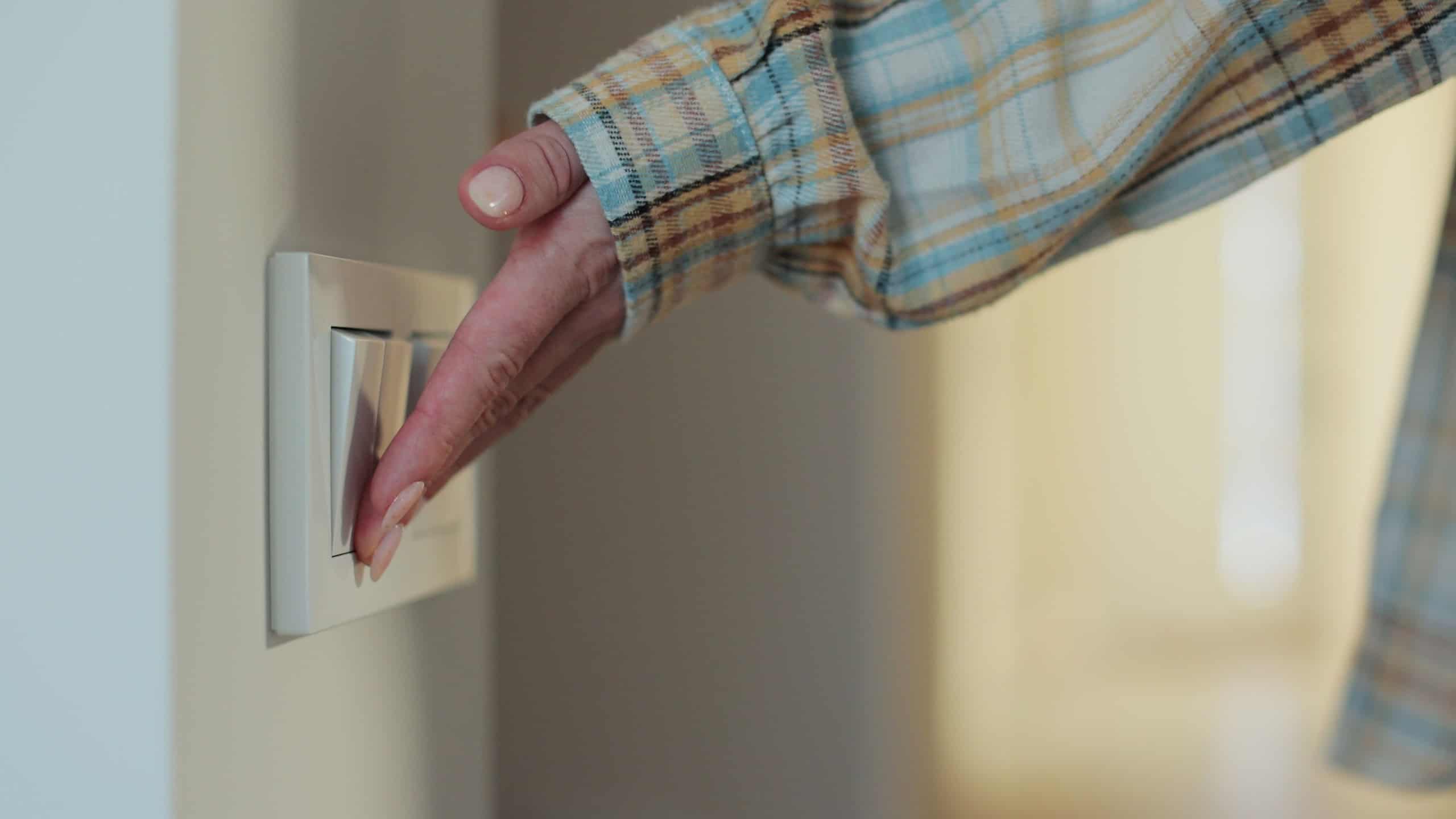 Close-up woman hand turns off light at home room by pressing a switch.