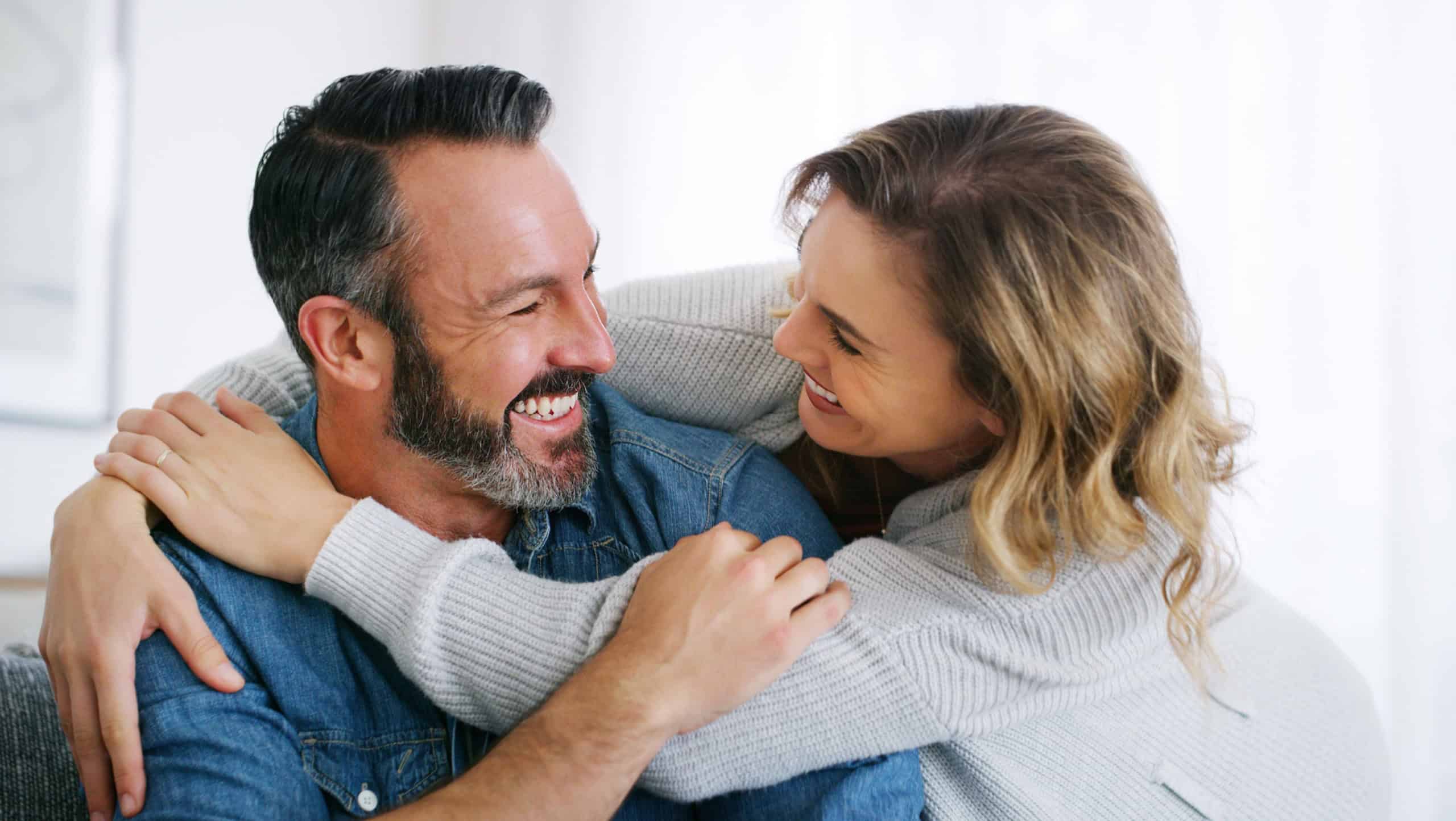 Relax, funny and hug with couple on sofa in home for bonding, connection and support. Weekend break, commitment and laugh with man and woman in living room of apartment for marriage together