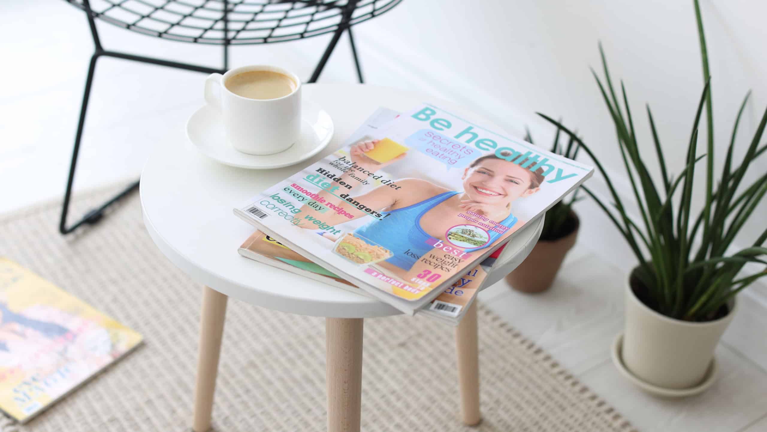 Lifestyle magazines and cup of coffee on white table indoors, closeup