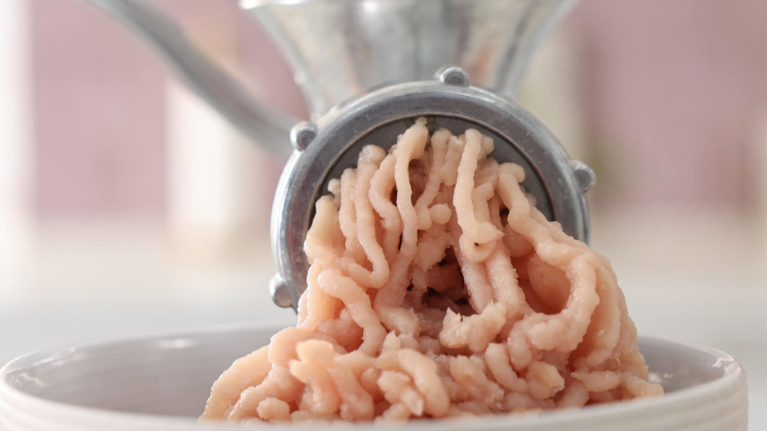 Manual meat grinder with chicken mince and ingredients on table in kitchen, closeup