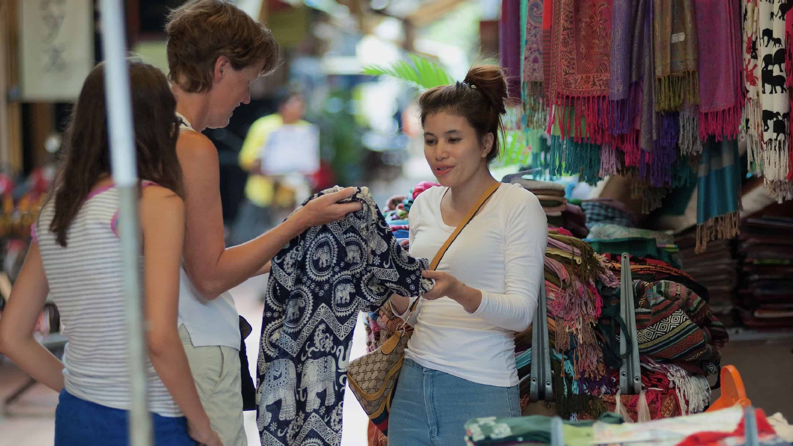 Unidentified European tourists bargain with a local seller over pants. Bargaining can reduce price several times.