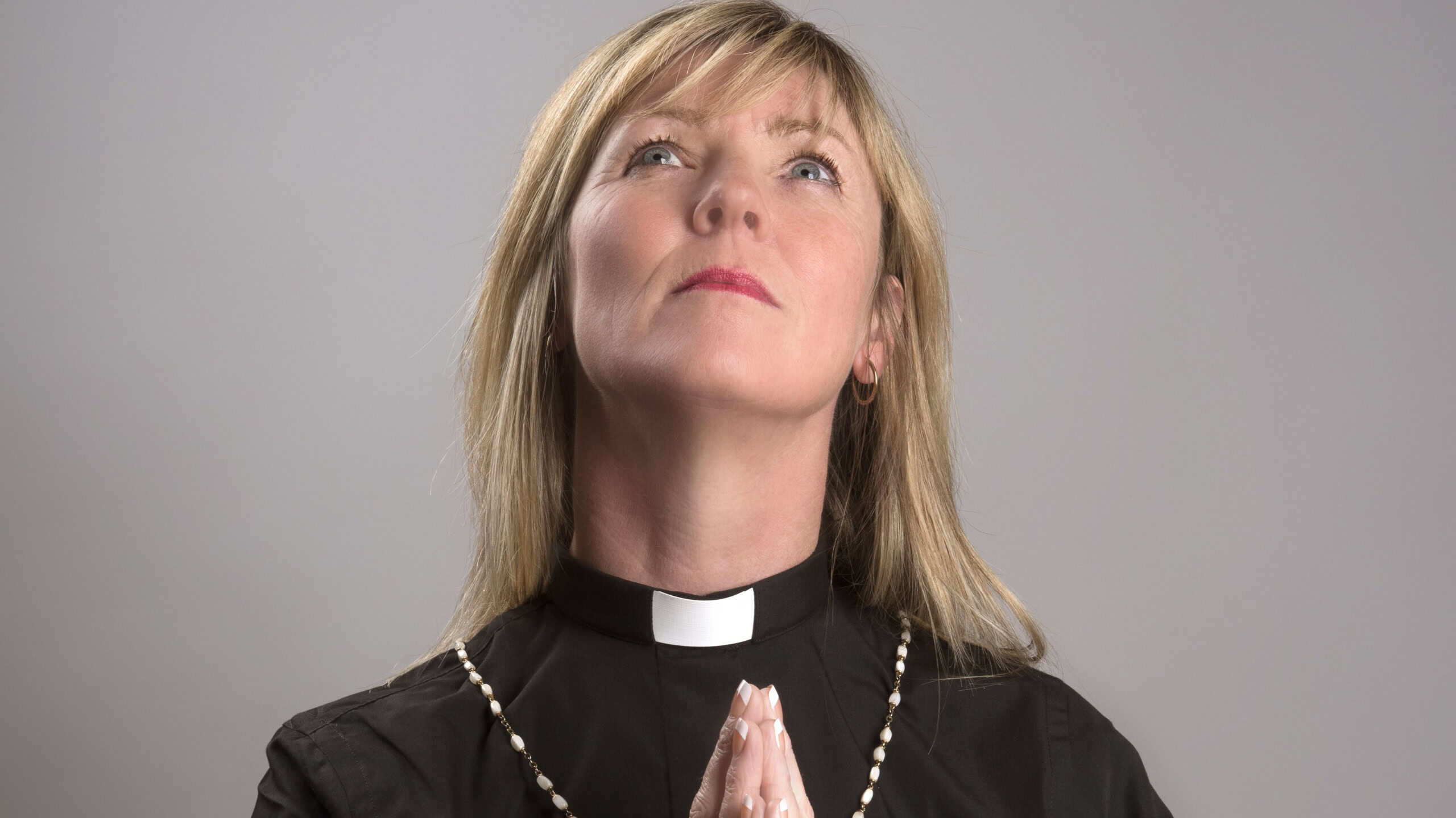 Portrait of a female clergy wearing a clerical collar,looking up and praying