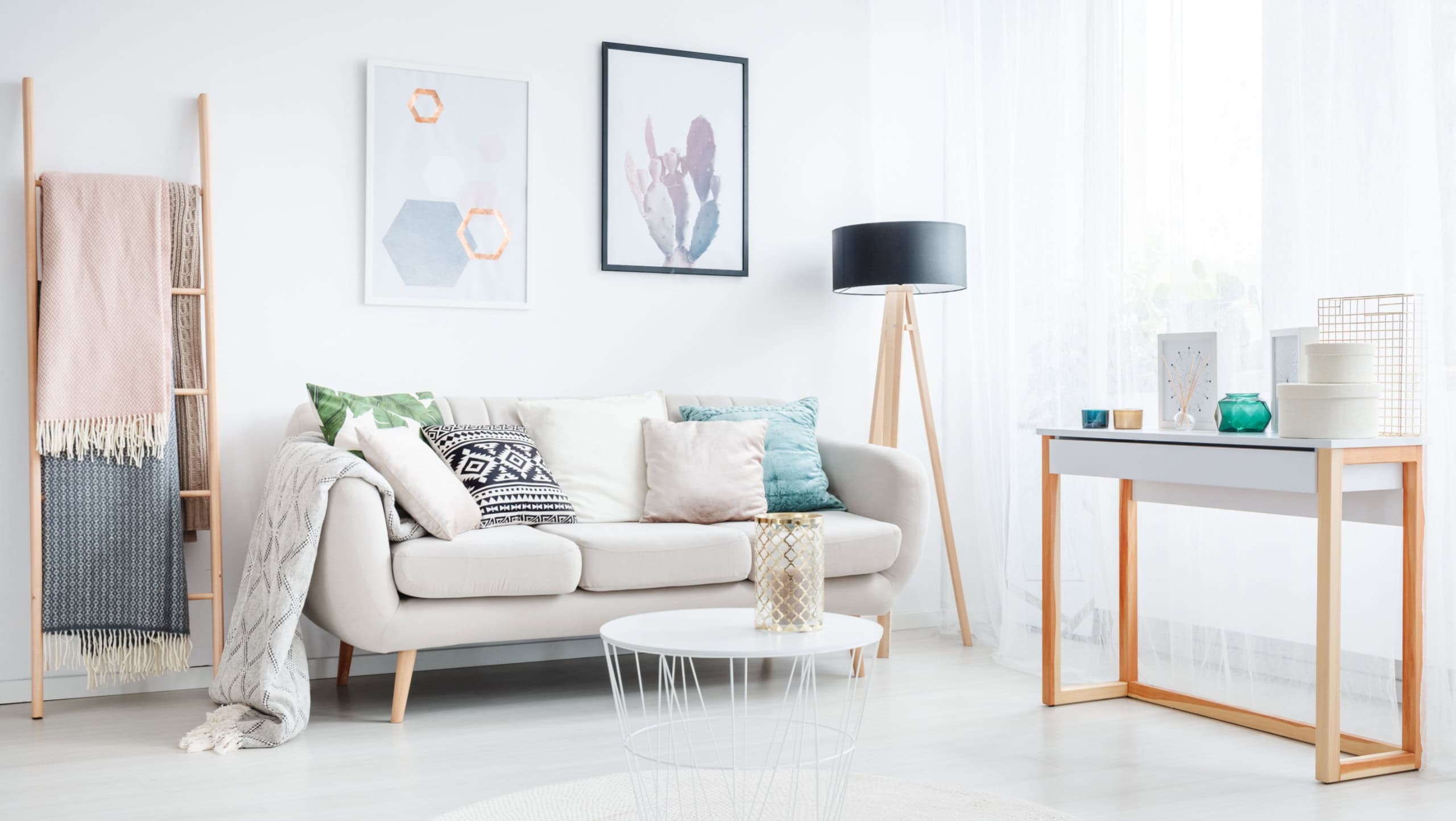 Blankets on a ladder and white table on a carpet in living room with lamp and cushions on a sofa