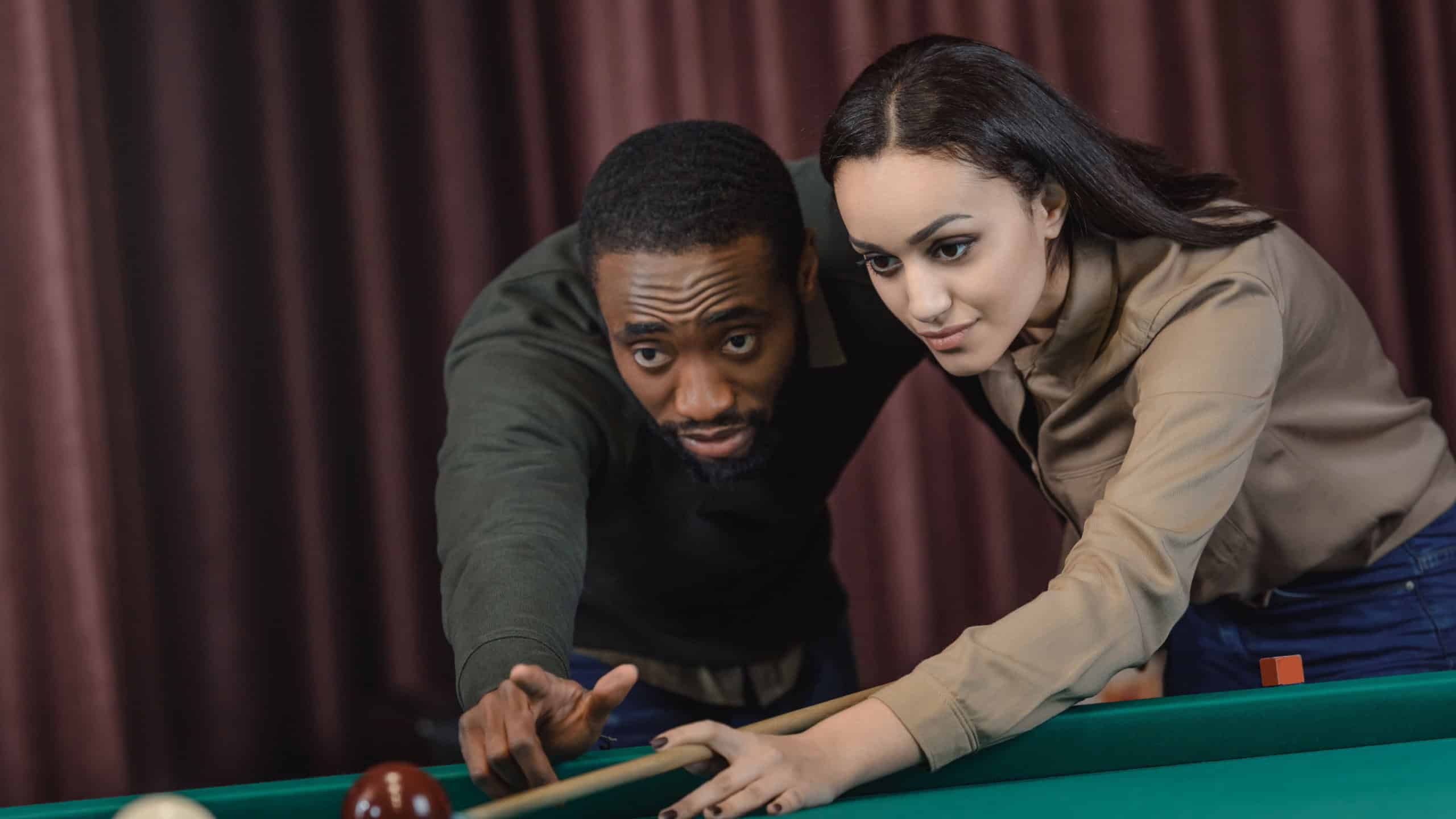 young attractive multiethnic man and woman playing in pool at bar