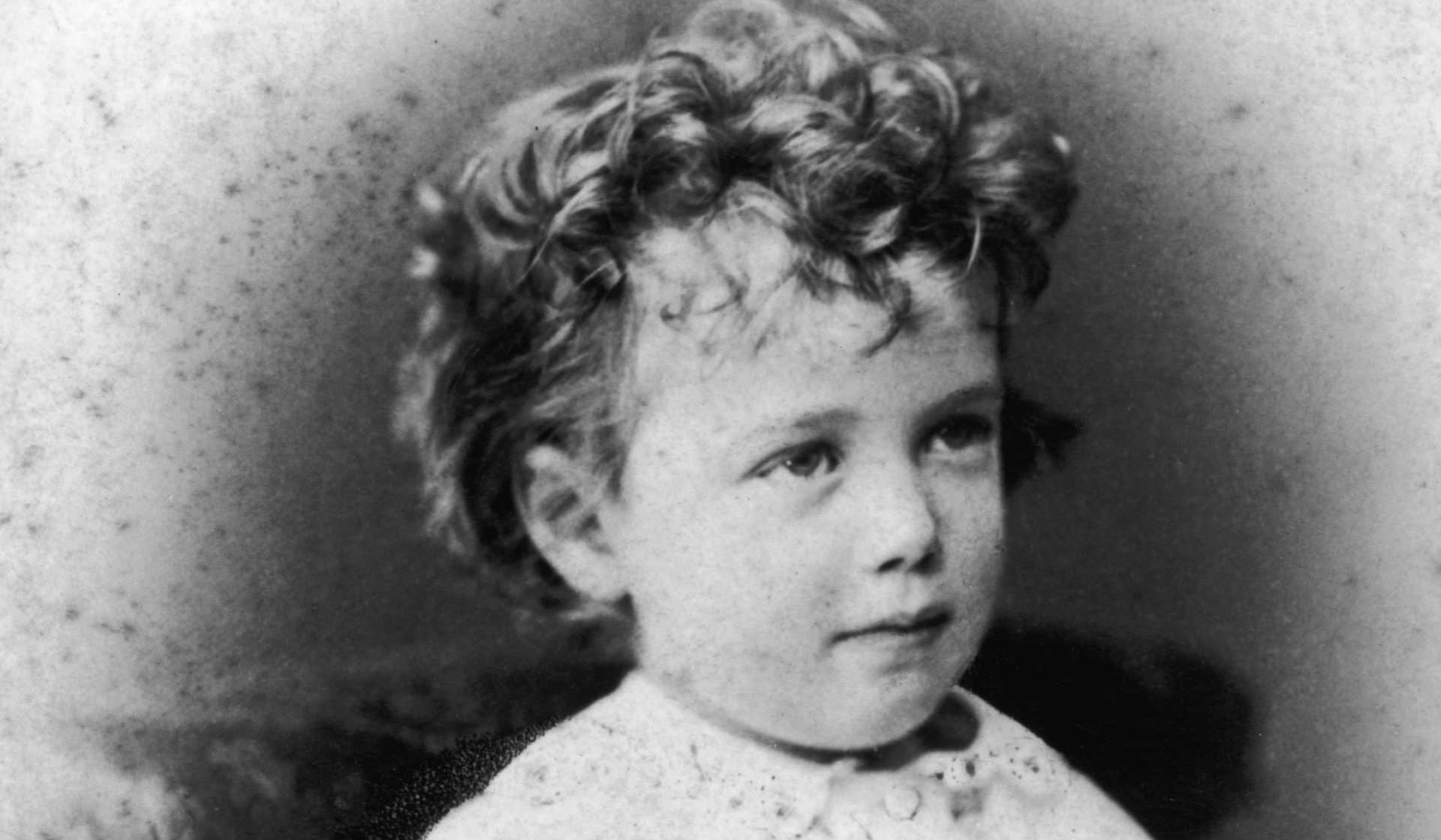 Black and white childhood portrait of a girl with curly hair and a serious expression.
