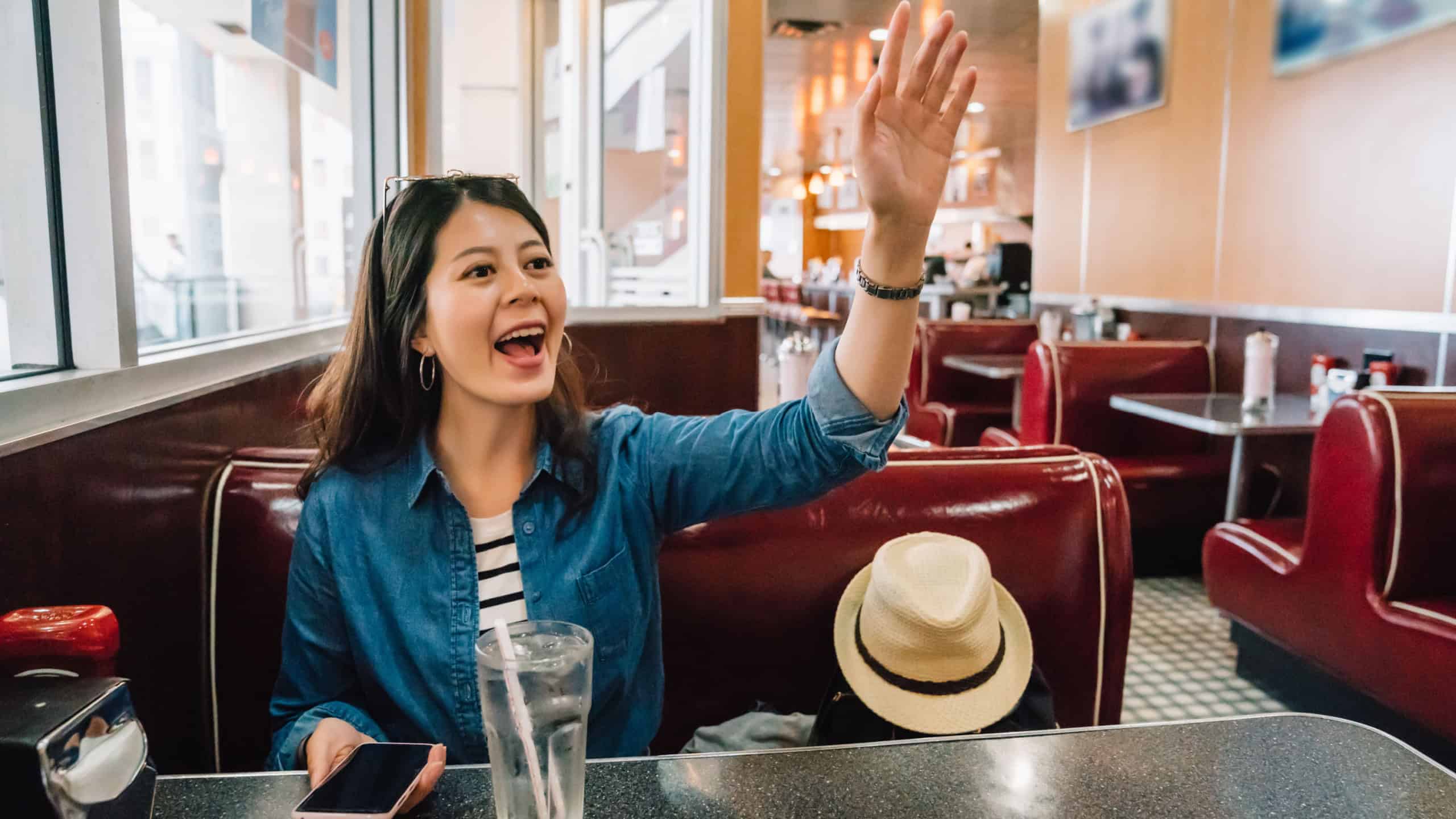 hungry lady cheerfully calling waiter to order food, because she finally find a restaurant to eat, young girl happy to see her friends show up and say hello.