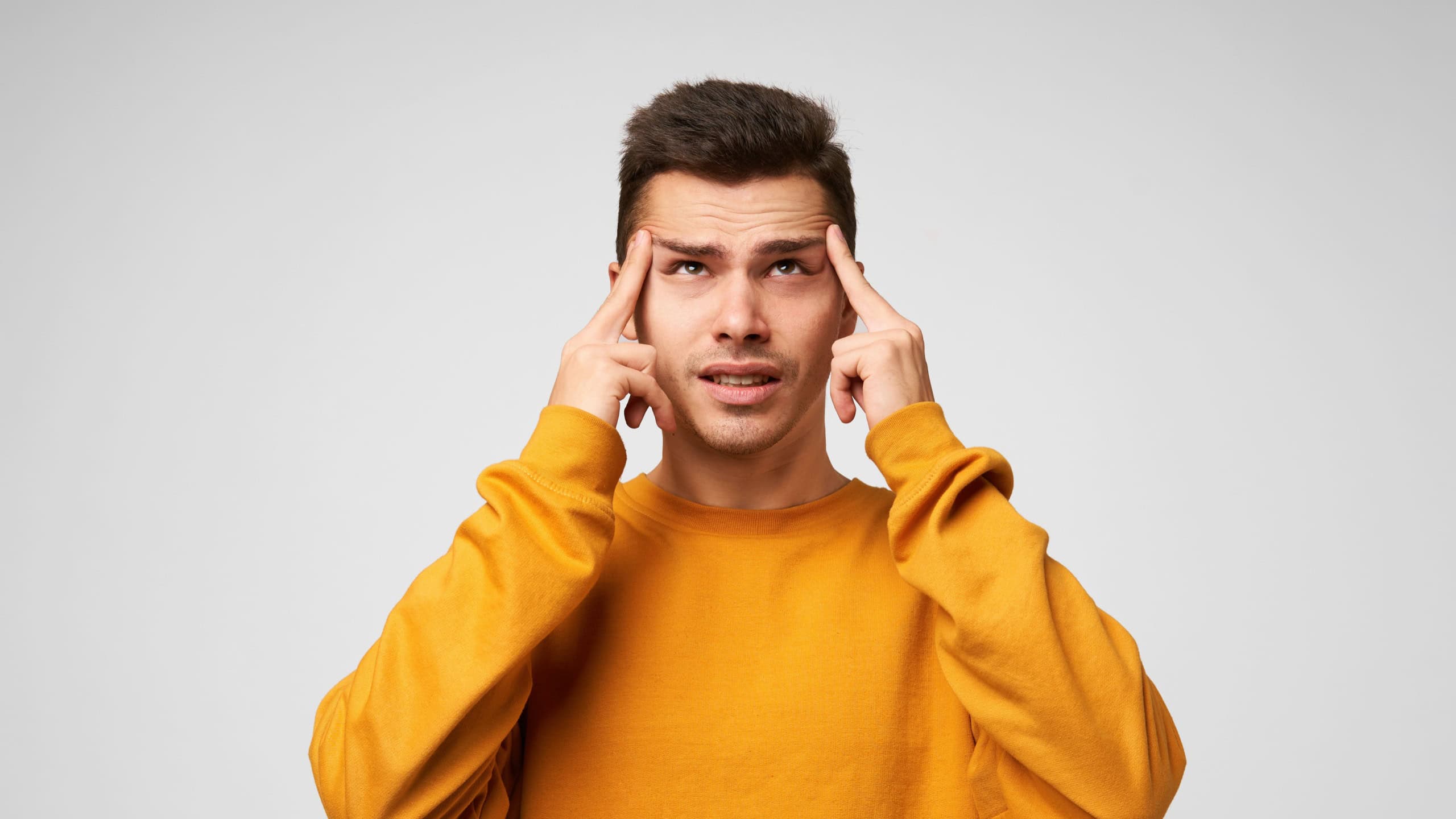 Young man ponders the idea, focused, looks up to the disytance, forefingers near temples, trying to remember something, immersed in thoughts, dressed casually, isolated over white background