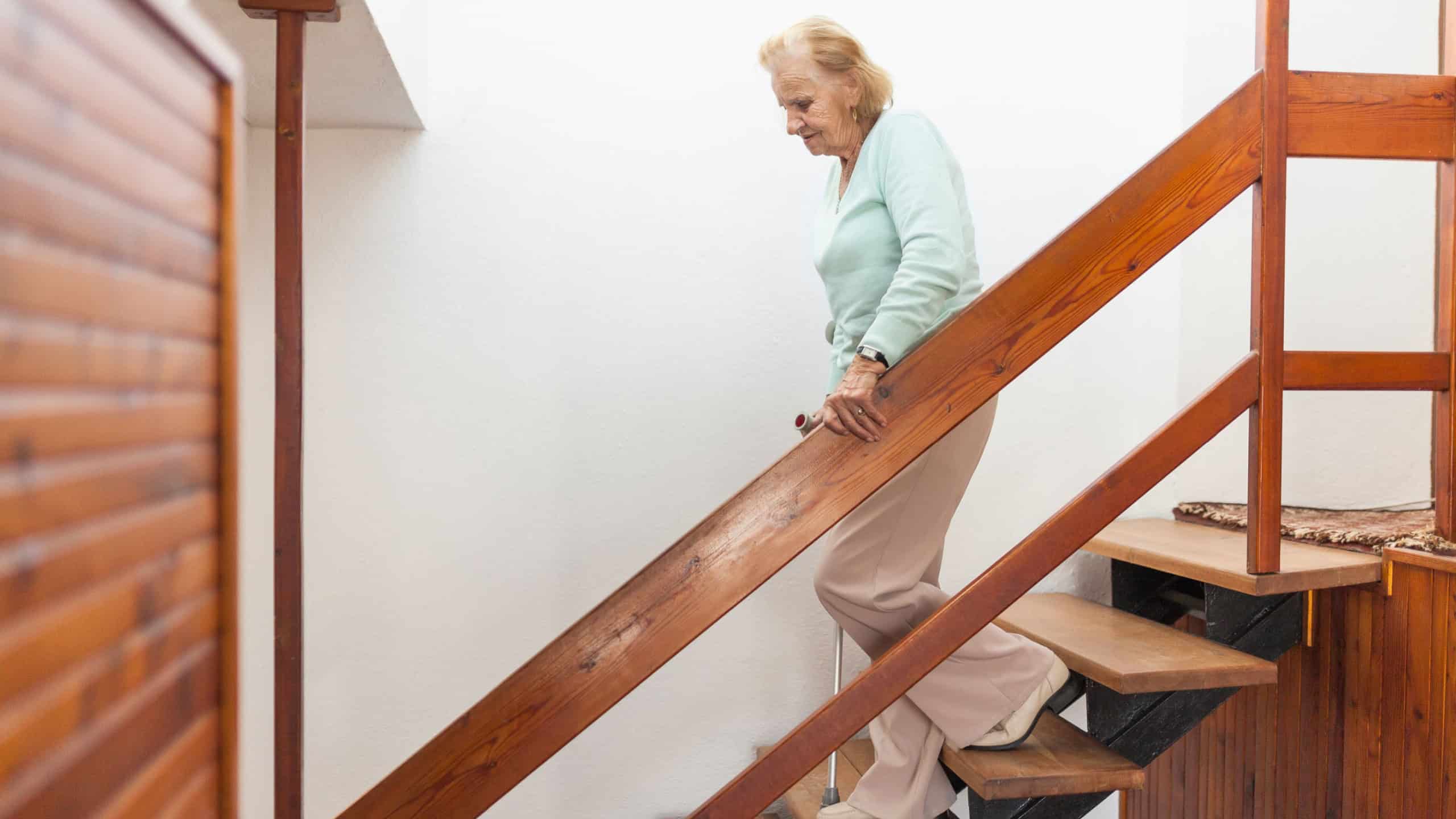 Elderly woman at home using a walking cane to get down the stairs