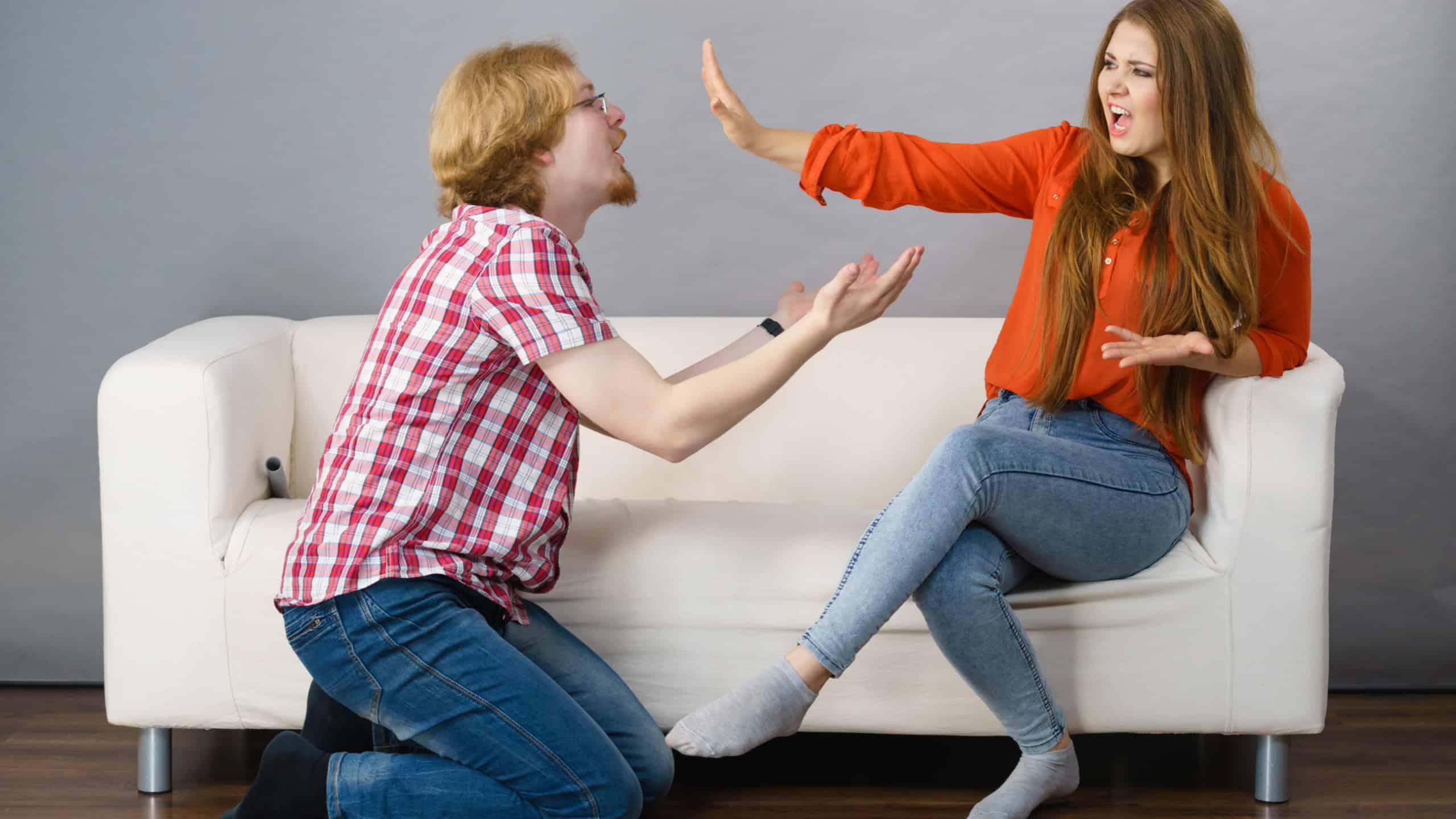 Man begging woman who is sitting on sofa for forgiveness. Couple after fight or argue. Female showing speak to hand