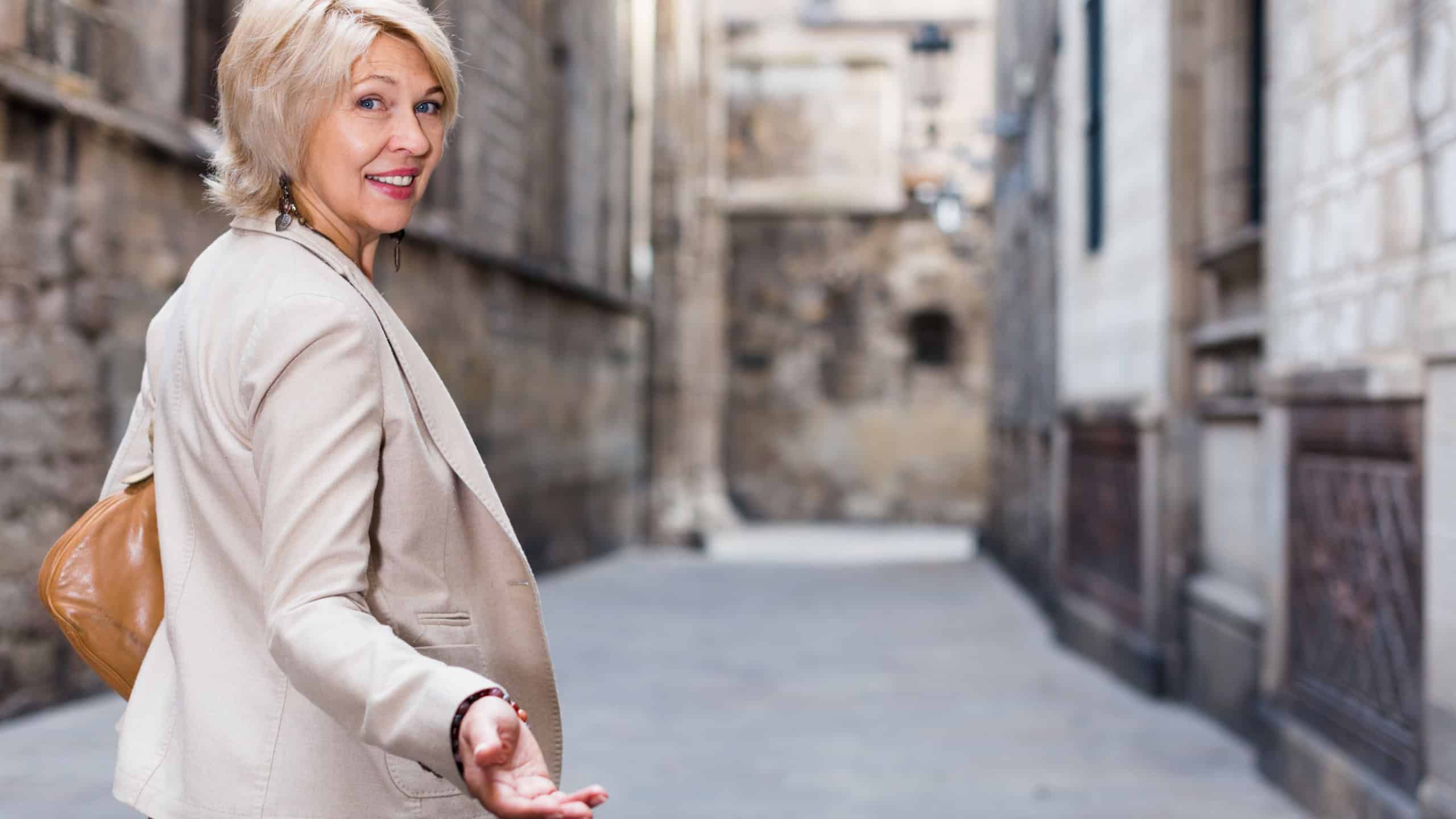 Adult woman 50s years old is walking in classic dress in old city.