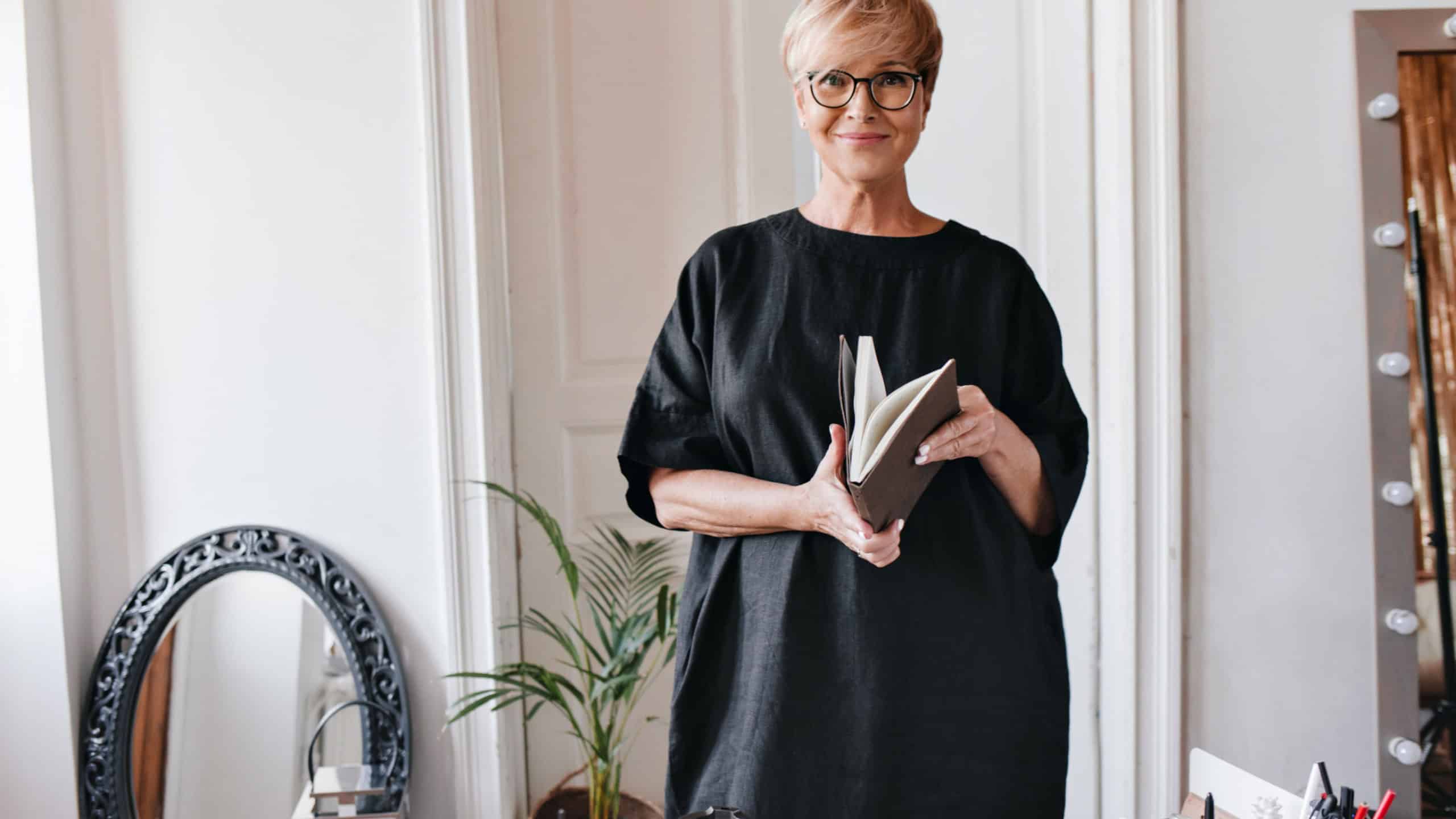 Beautiful lady in oversized dress looks into camera and holds notebook