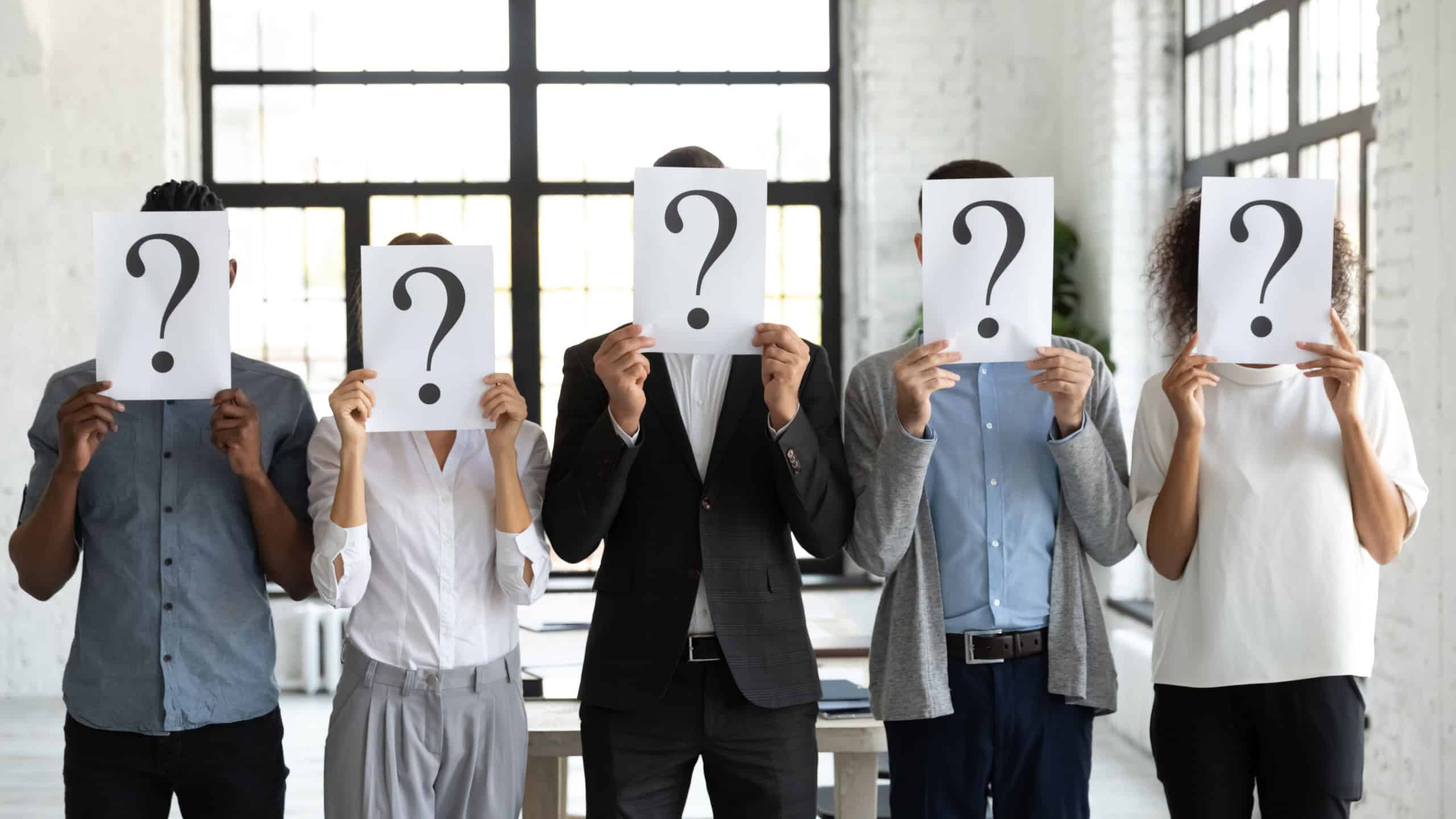Diverse business people hiding faces behind papers sheets with question marks, standing in row in office. Identity and equality employee at work, candidates waiting for job interview, recruitment.