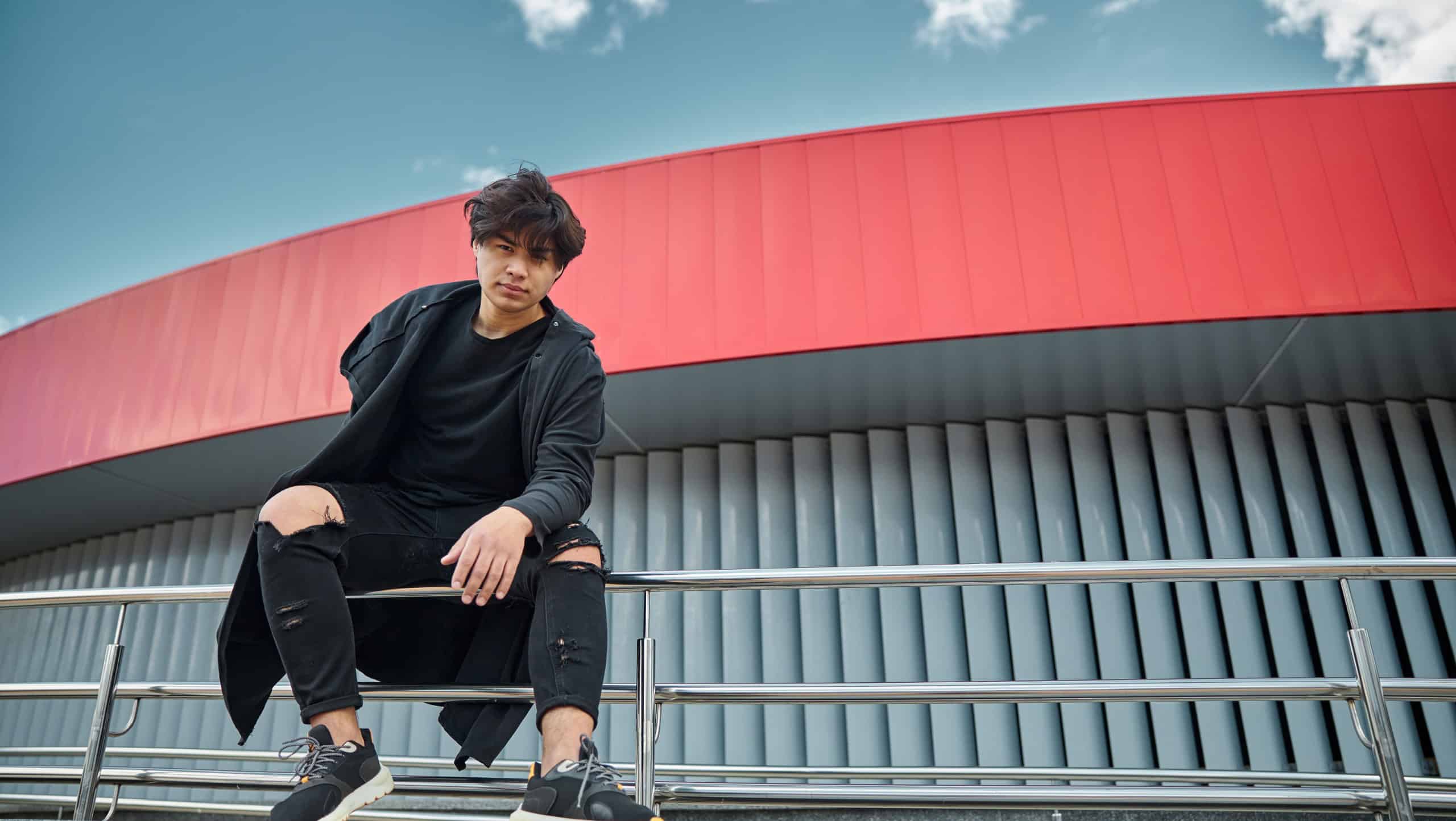 Attractive guy in stylish black outfit looking at camera with serious expression while spending time outdoors