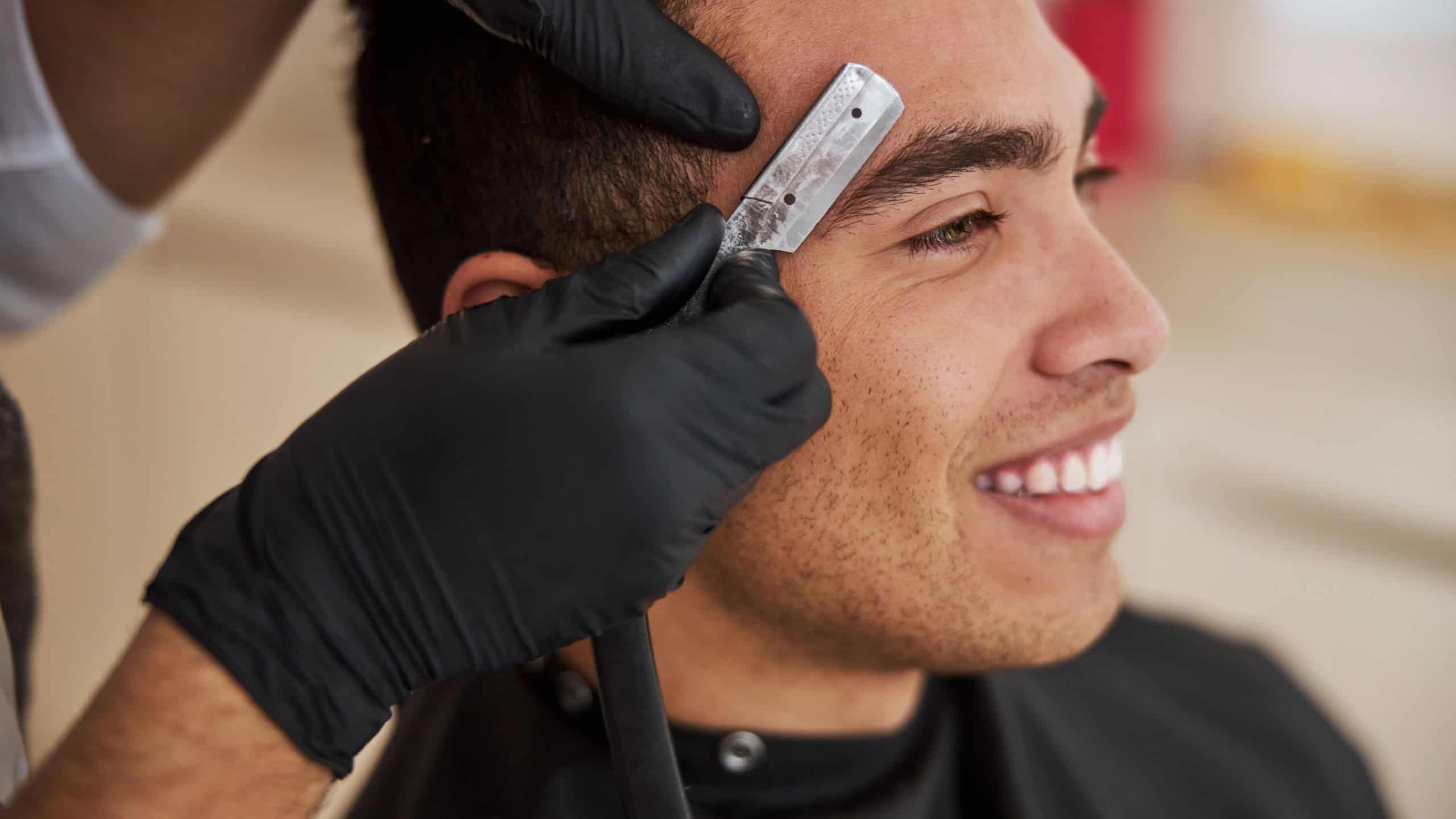 close up side view portrait of happy attractive male sitting in beauty salon while barber making eyebrow styling