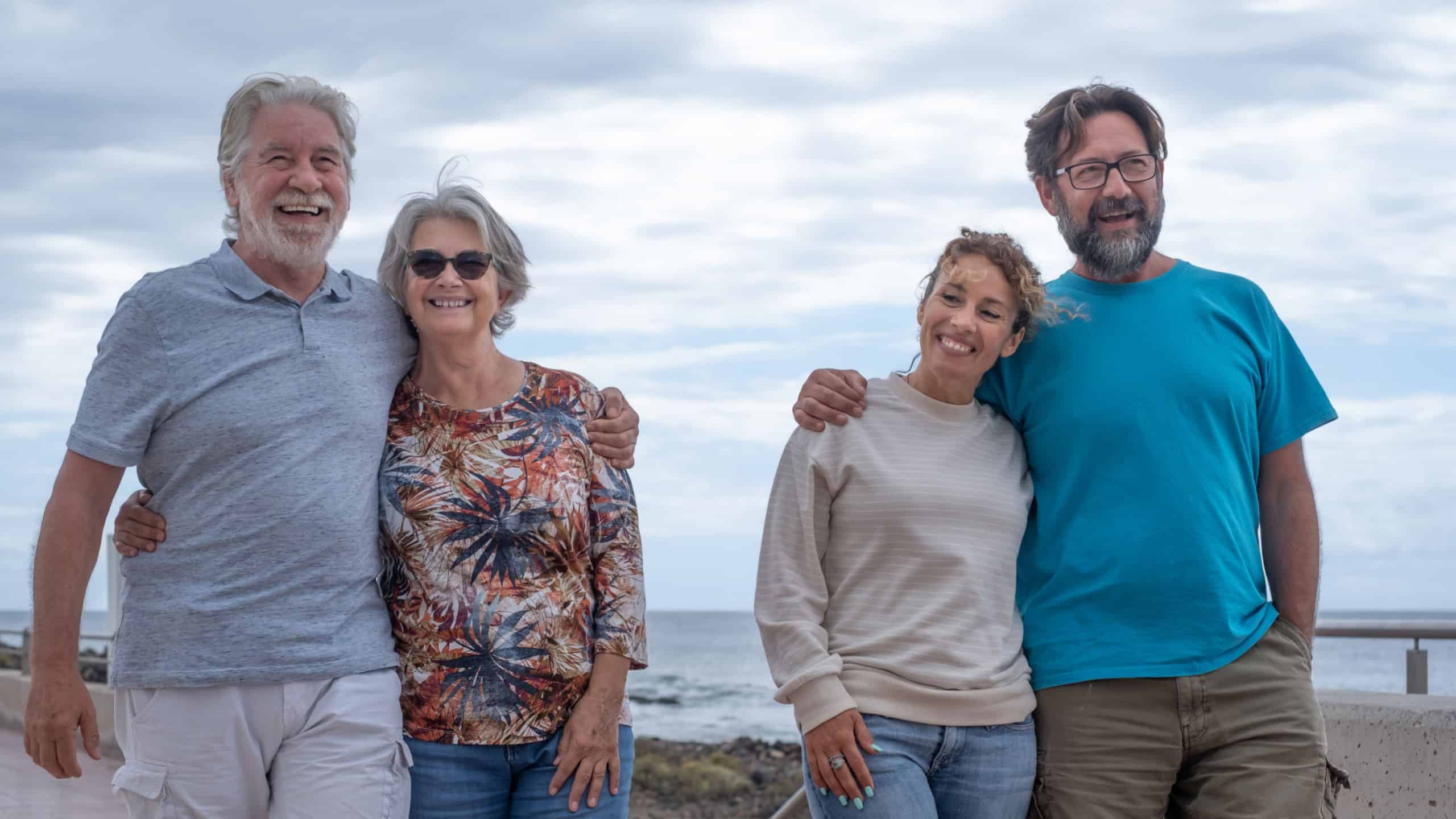 Two married couples, of different ages, stroll together along the sea, smiling carefree