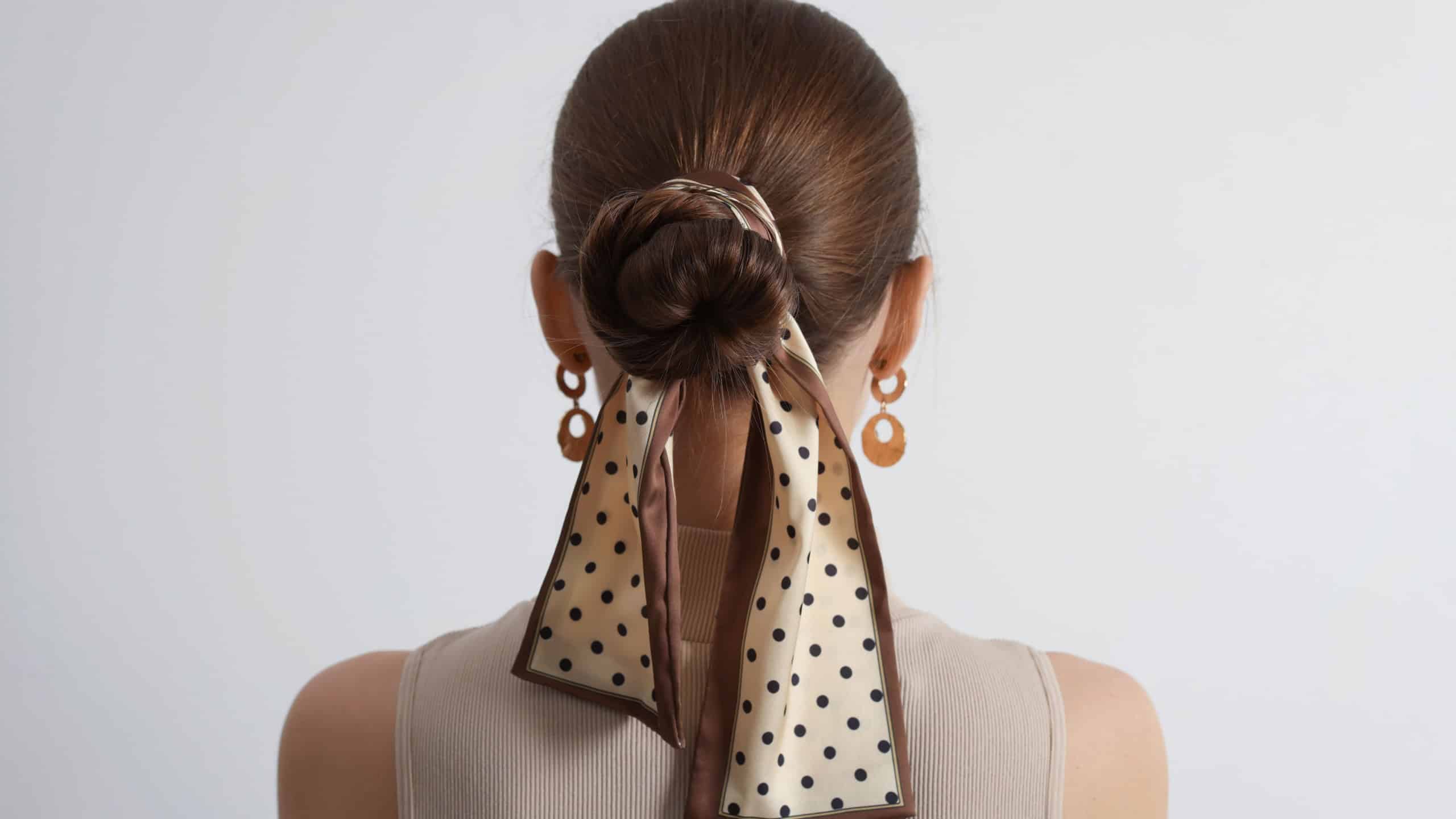 Young woman with stylish bandana on light background, back view