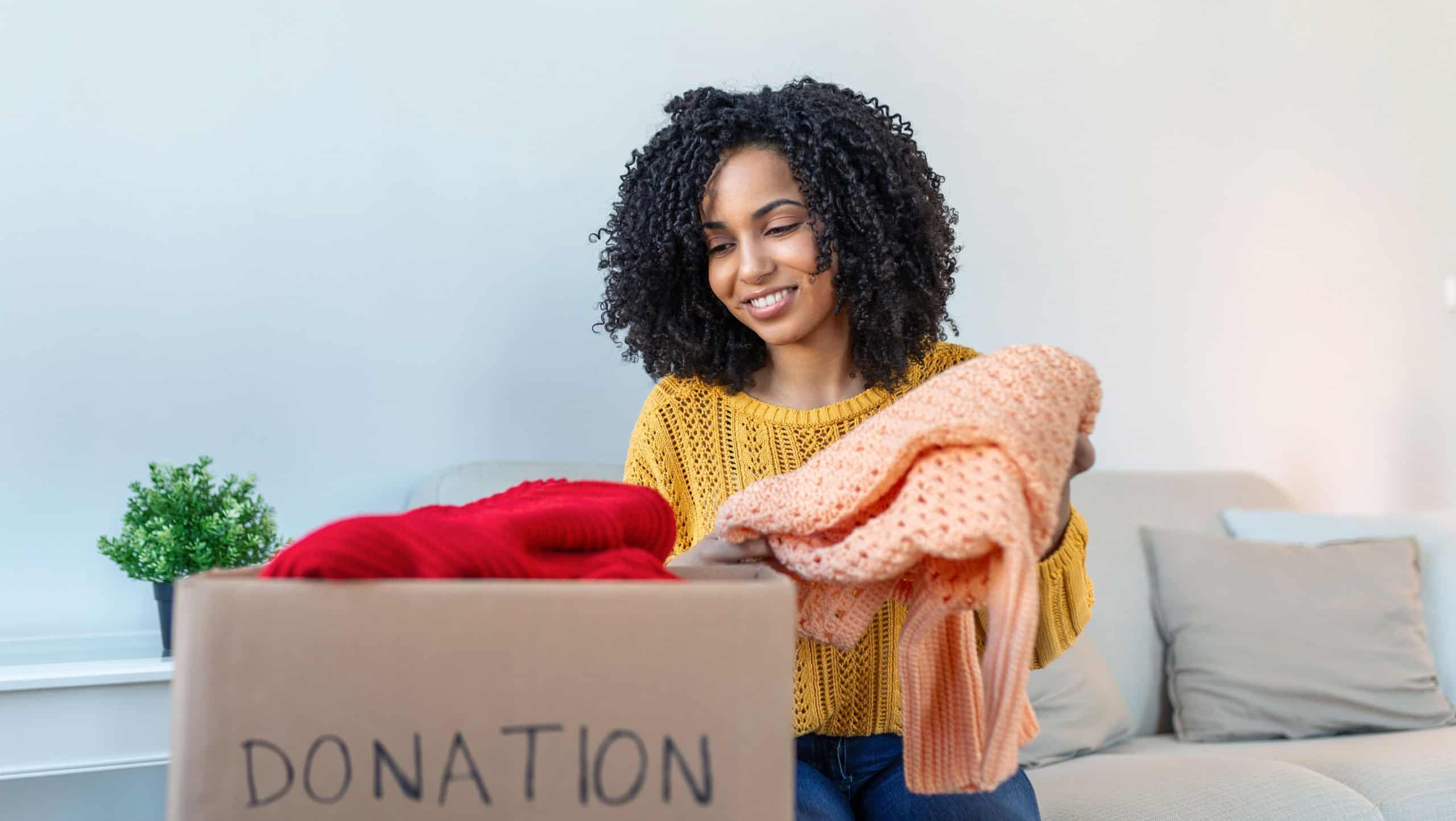 Woman holding cardboard donation box full with clothes. Concept of volunteering work, donation and clothes recycling. Helping poor people