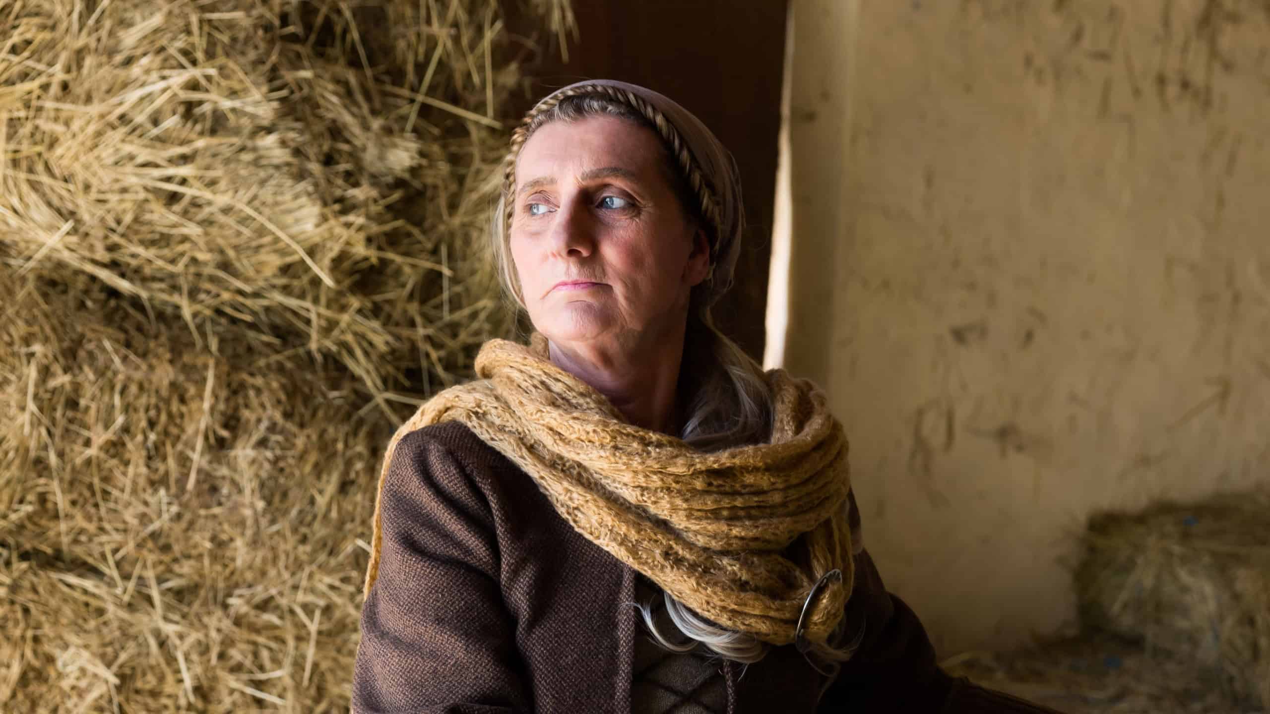 Woman in historical medieval costume posing with a wicker basket in a hay barn