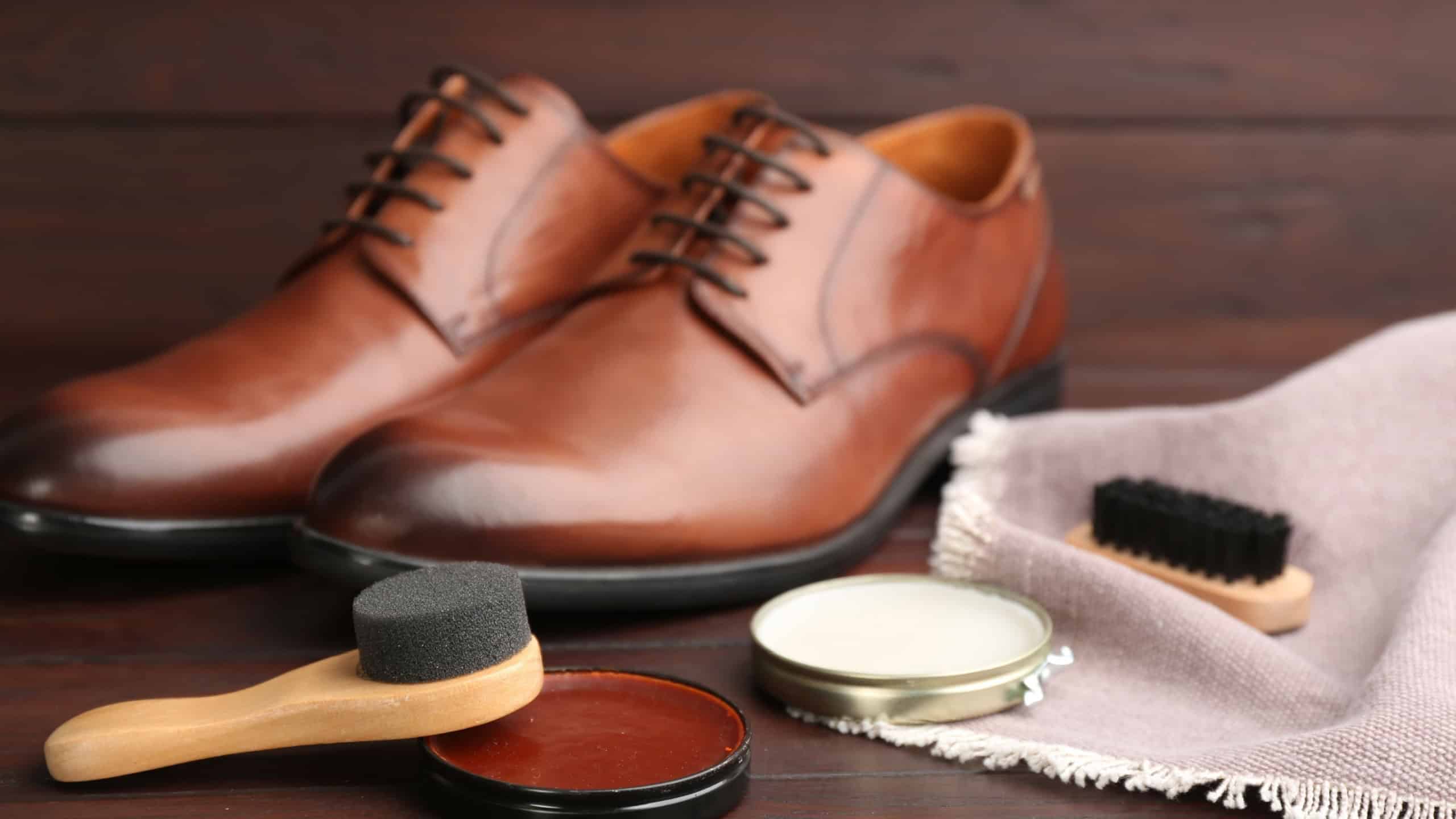 Shoe care products and footwear on wooden table, closeup