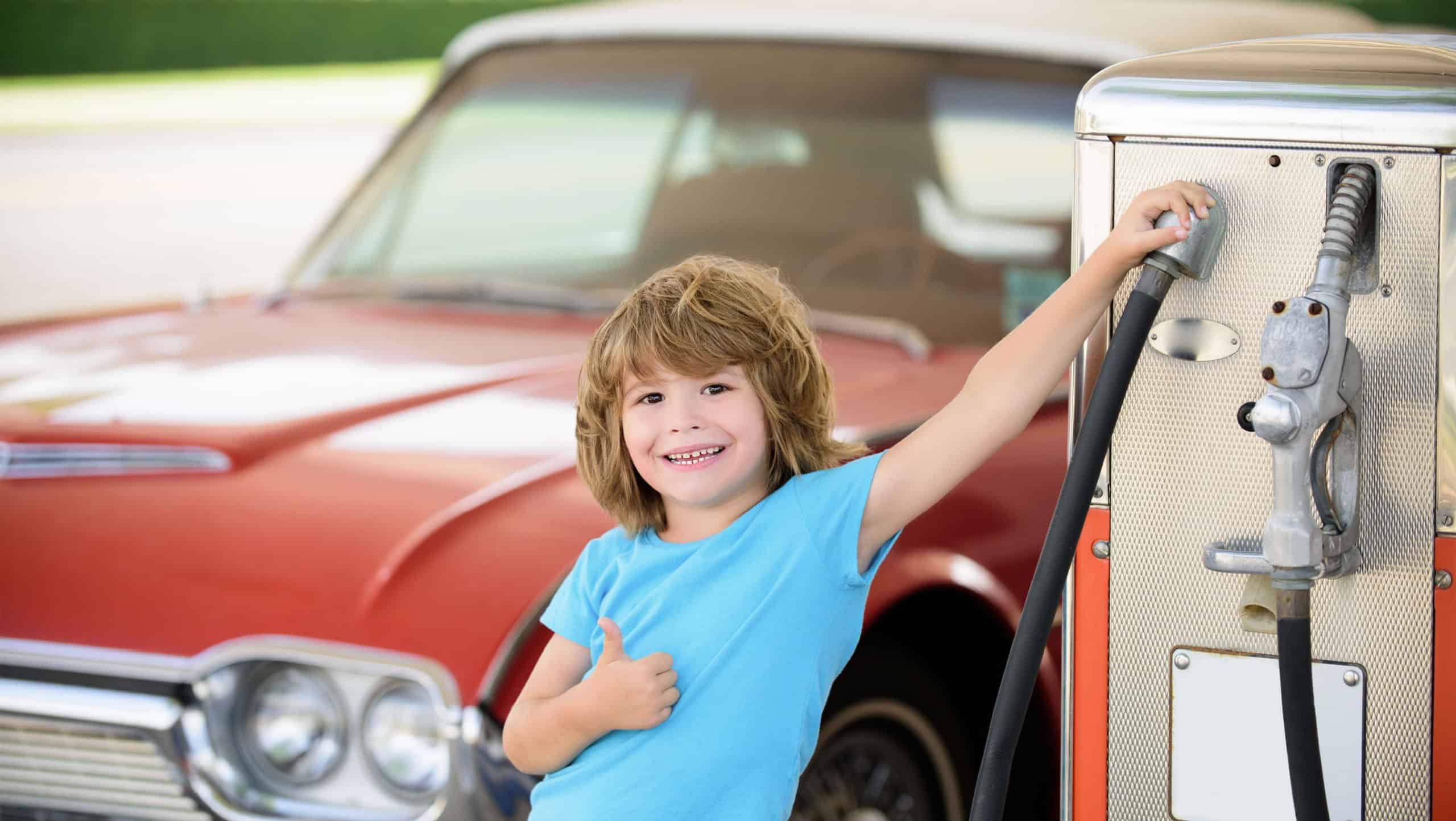 Child at gas station against red retro automobile.