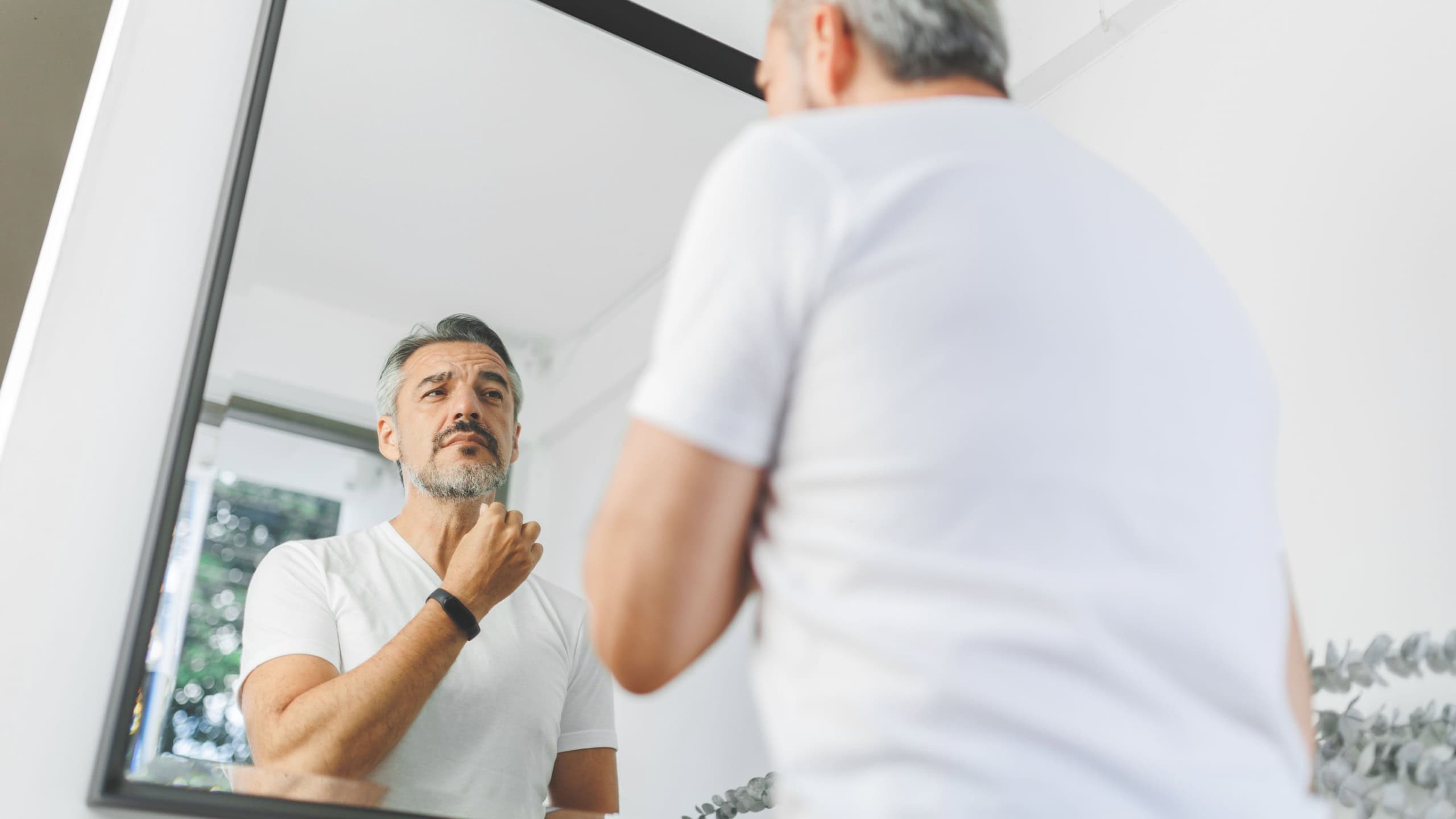 Portrait of handsome Mature adult man touching his beard and looking at his reflection in mirror