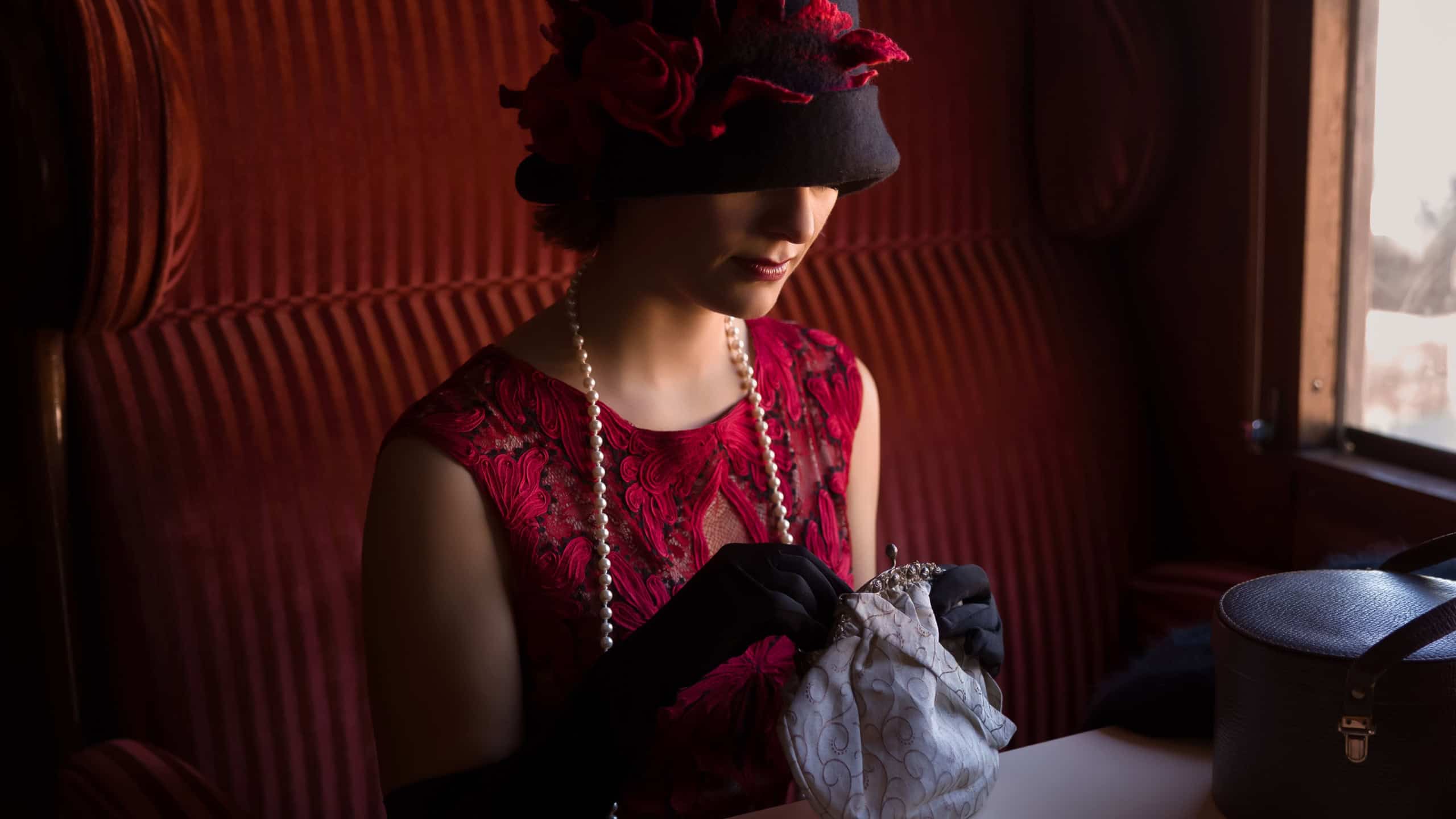 Attractive 1920s woman in red flapper dress and cloche hat posing in the 1927 first class interior of an authentic steam train
