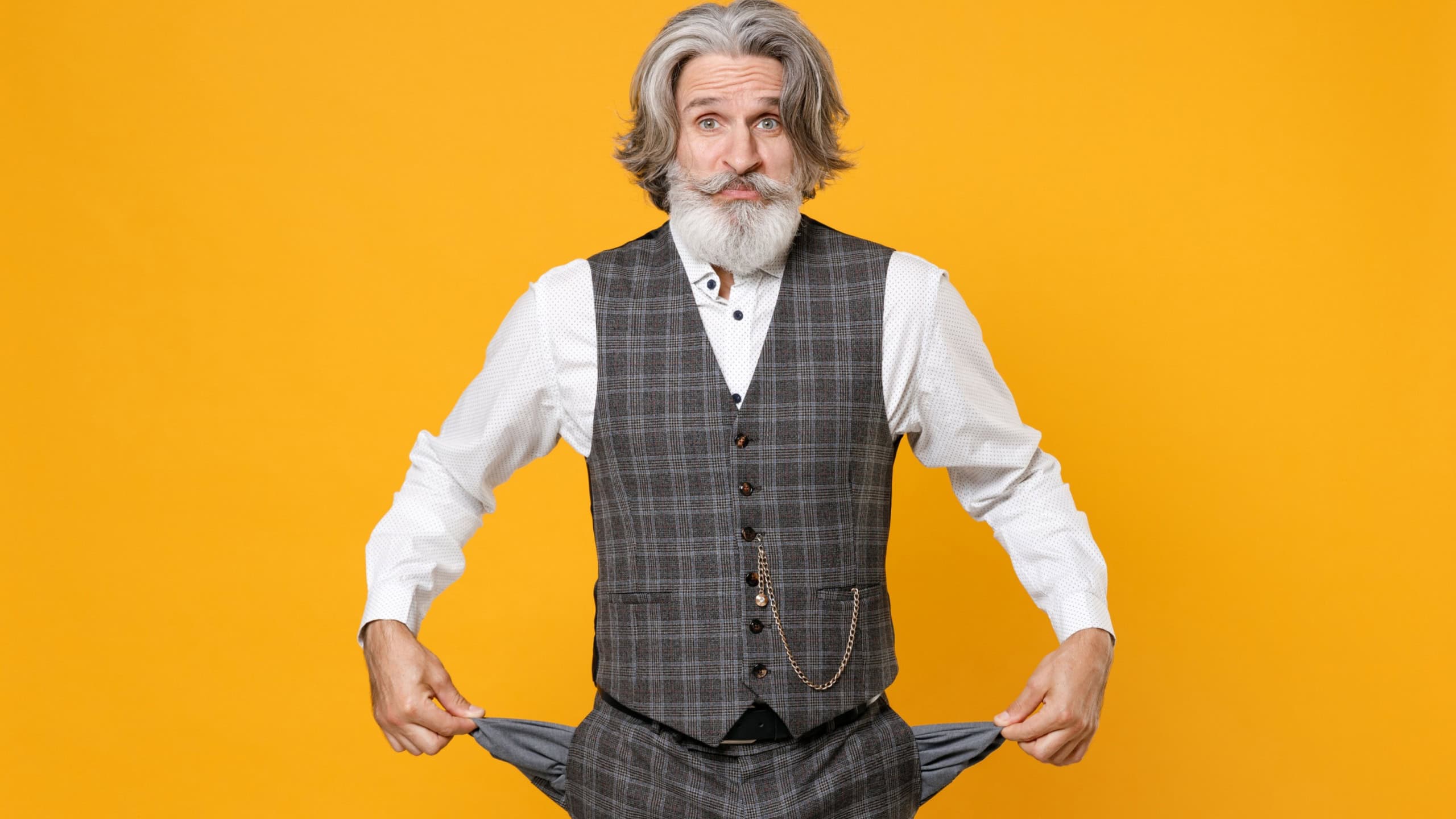 Confused elderly gray-haired bearded business man in checkered suit waistcoat shirt has no money showing empty pockets isolated on yellow background studio portrait. Achievement career wealth concept