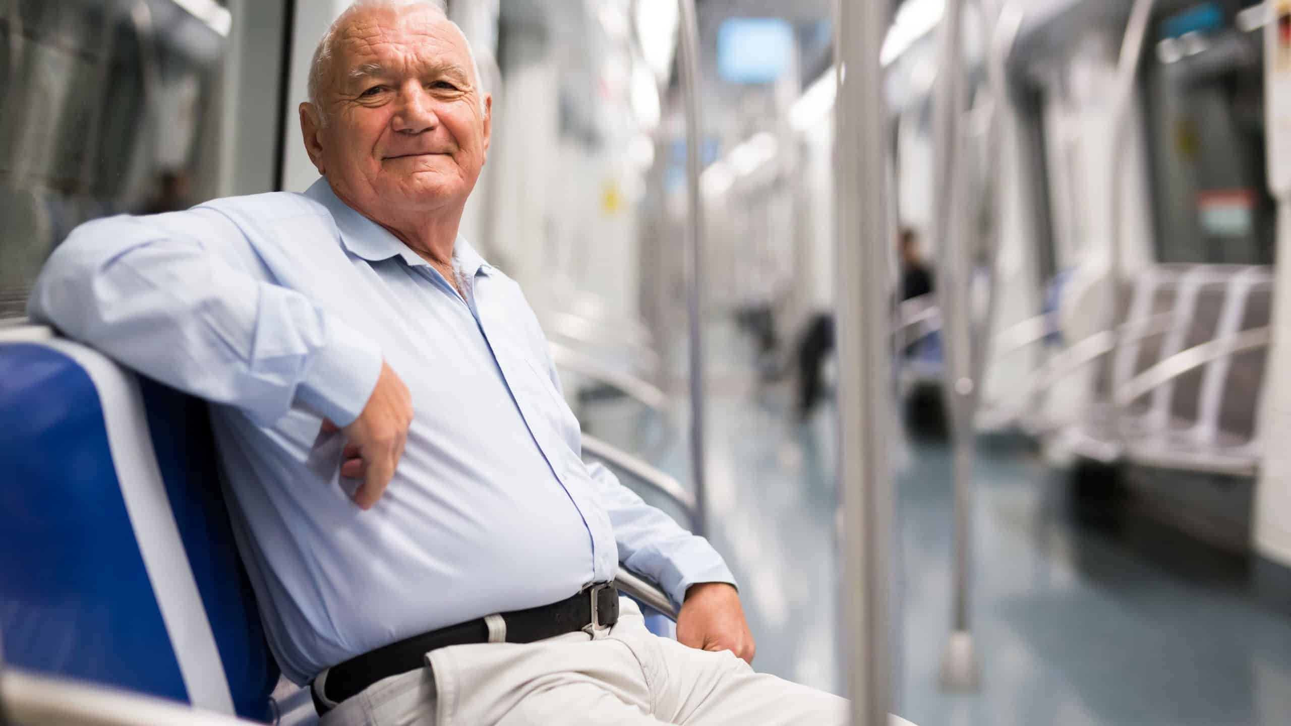 Senior Caucasian man sitting on seat in subway car and looking in camera.