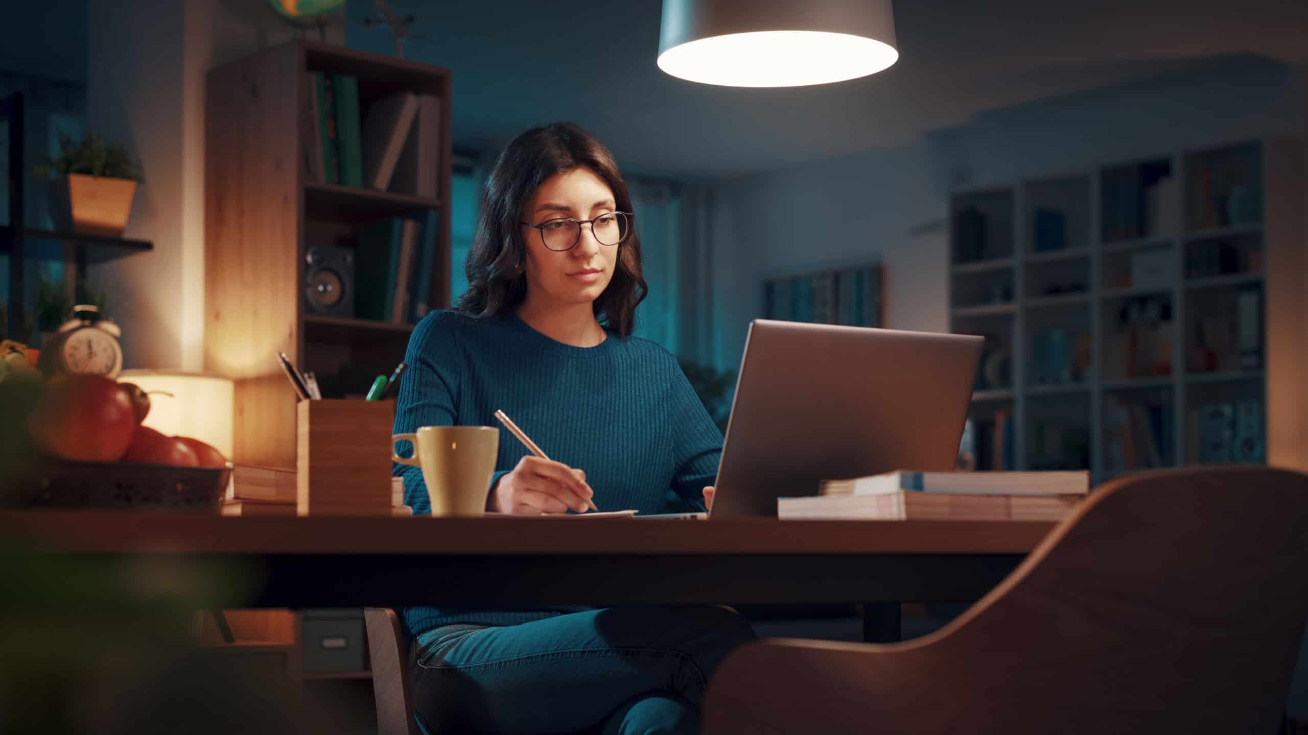 Woman sitting at her desk and connecting with her laptop late at night, she is studying and attending online classes