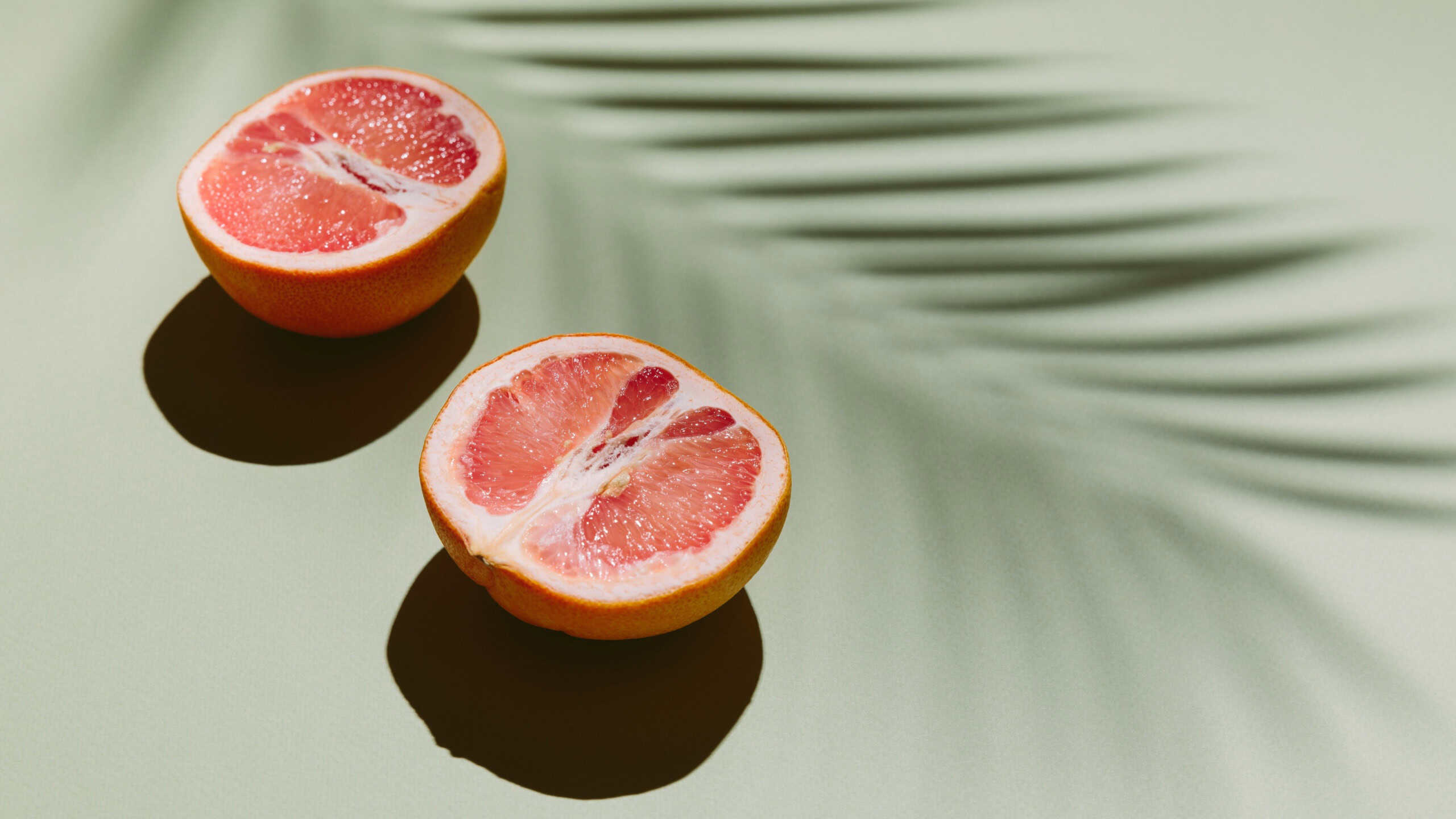 Fresh healthy grapefruit slices on green background with palm leaf shadow. Creative minimal concept, summer food, vacation, holiday. Flat lay, copy space