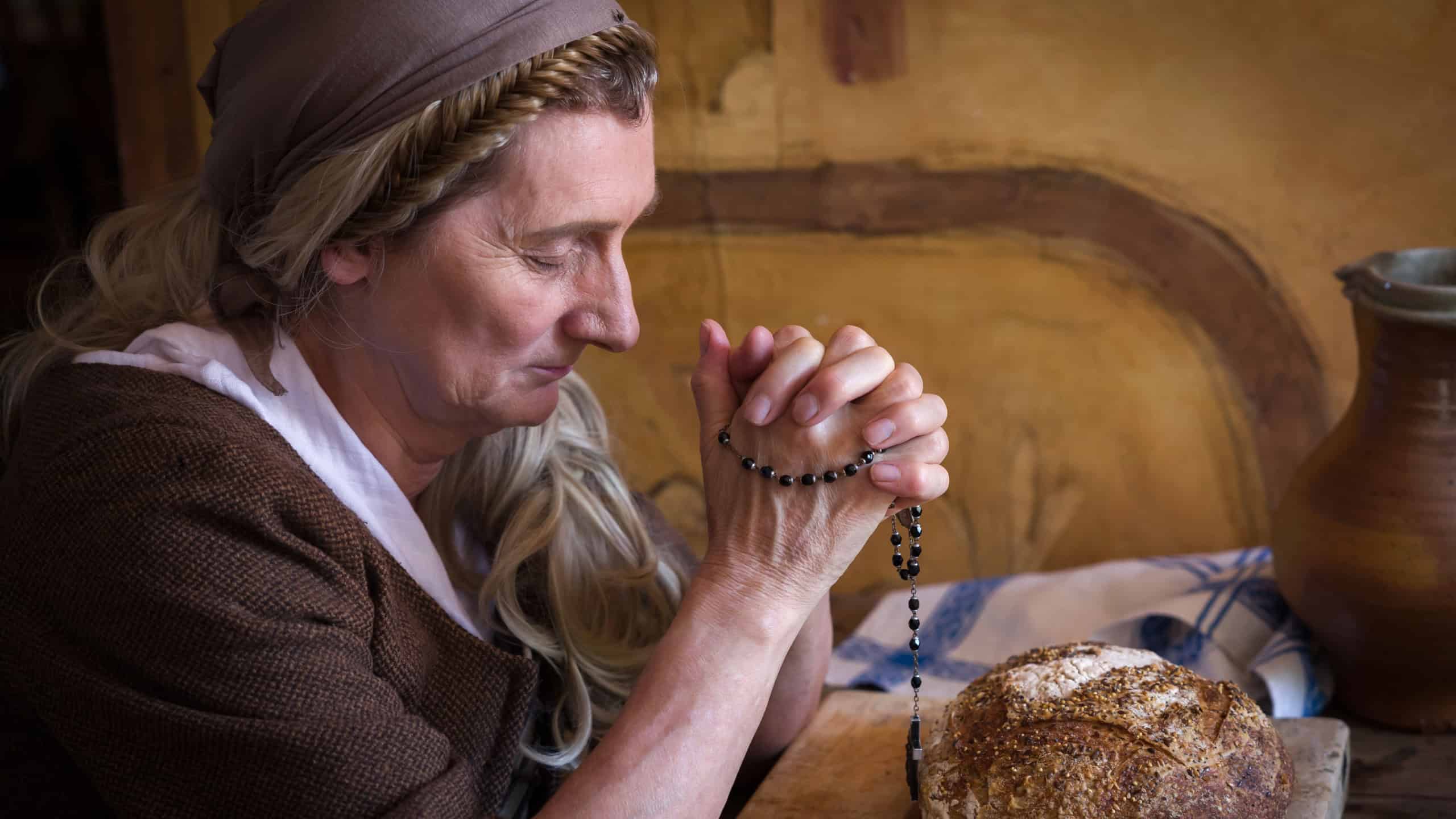 Woman in authentic peasant renaissance costume praying at a table. There is bread on the table.