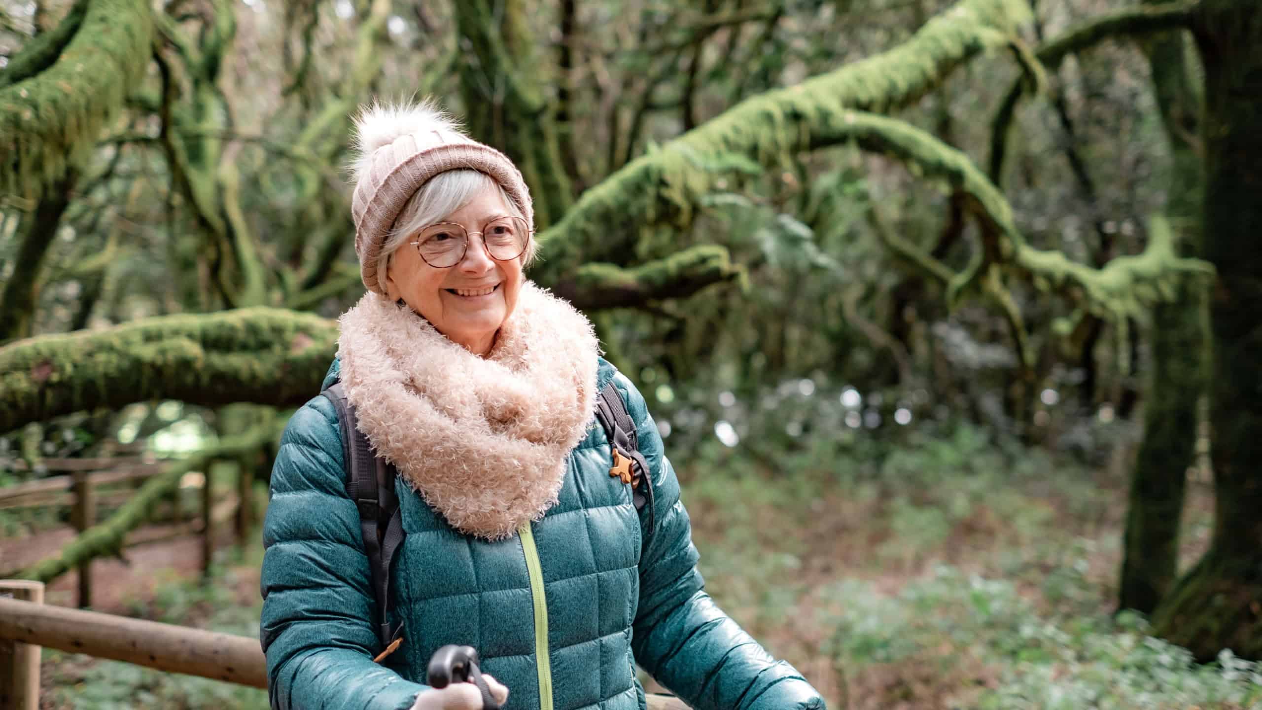 Carefree smiling senior woman holding backpack walks in the Garajonay national park in La Gomera. Elderly active woman hiking in mountain forest enjoying nature and healthy lifestyle