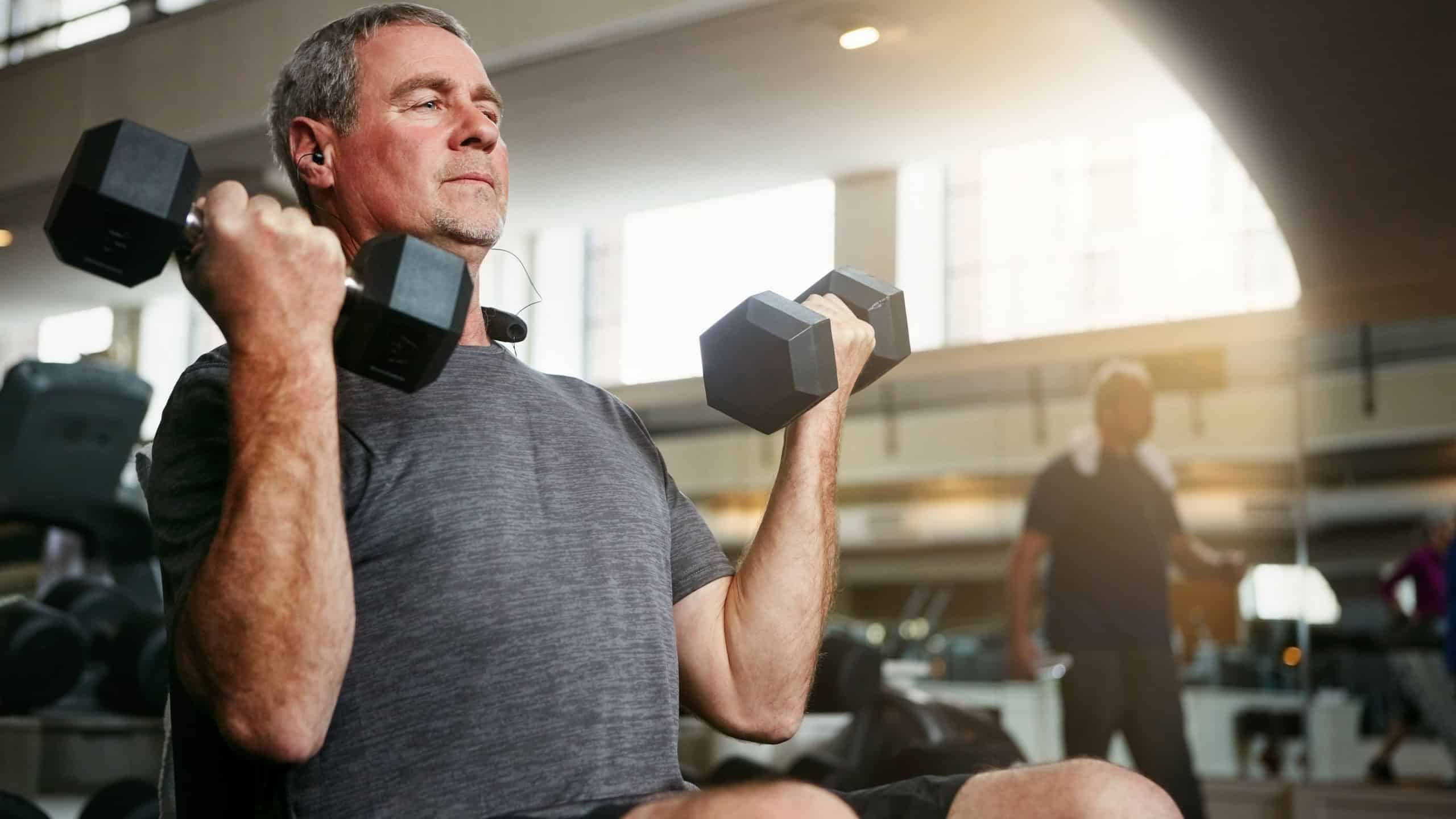 Fitness, gym and senior man with dumbbells for weightlifting, challenge or cardio workout, training or bodybuilding. Biceps, arms and elderly person with hand weight for strength, mindset or exercise