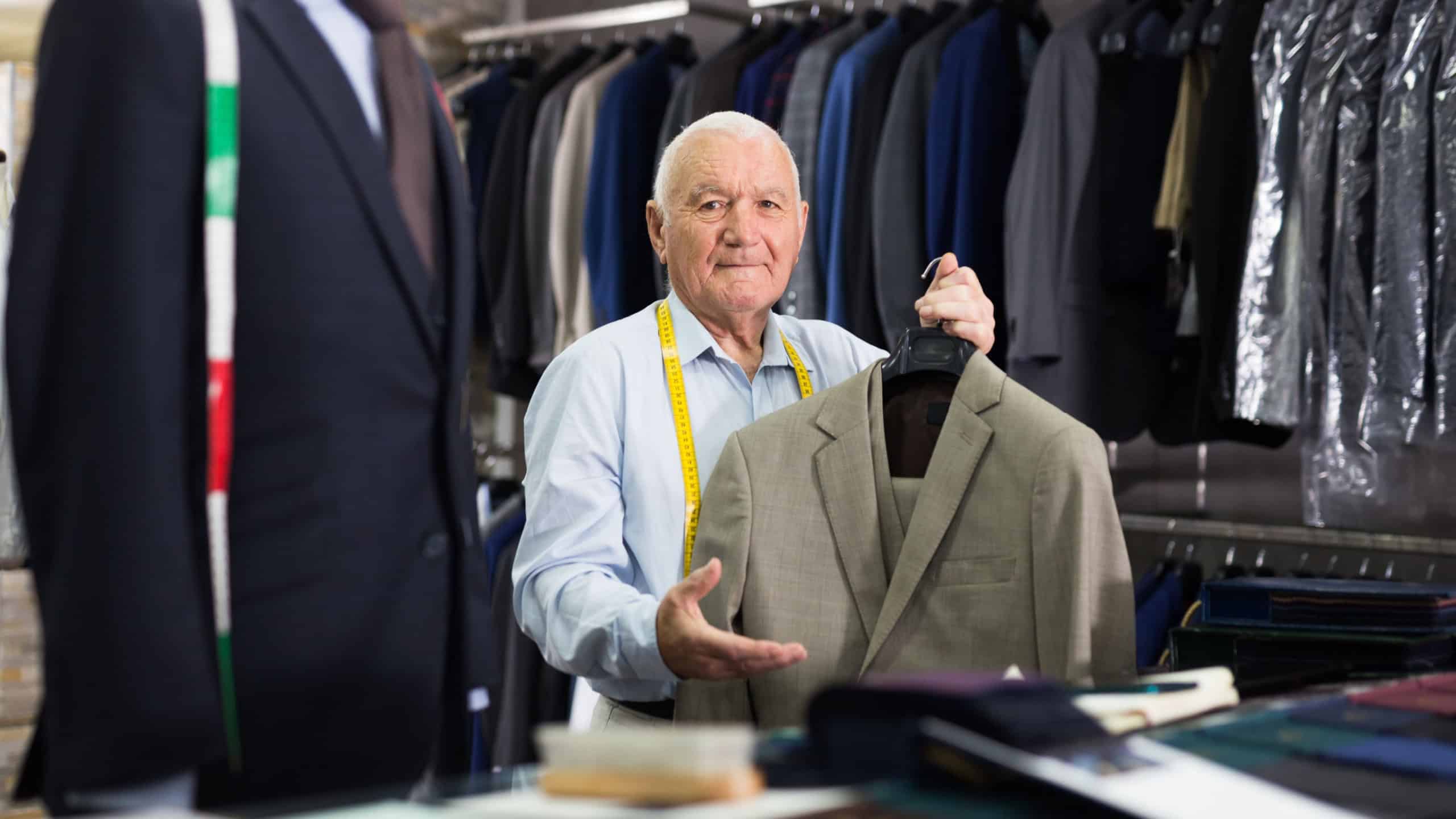Mature male tailor demonstrating of fashionable suit in apparel shop