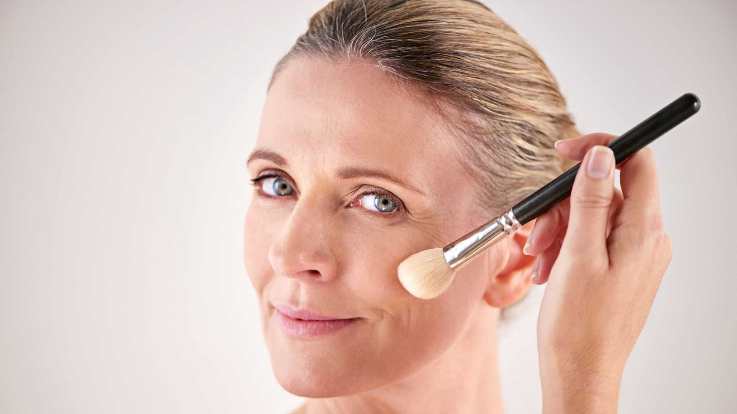Brush, cosmetics and portrait of woman in studio for makeup, self care and facial flow routine. Beauty, foundation and female person with cosmetology tool for face treatment by gray background.