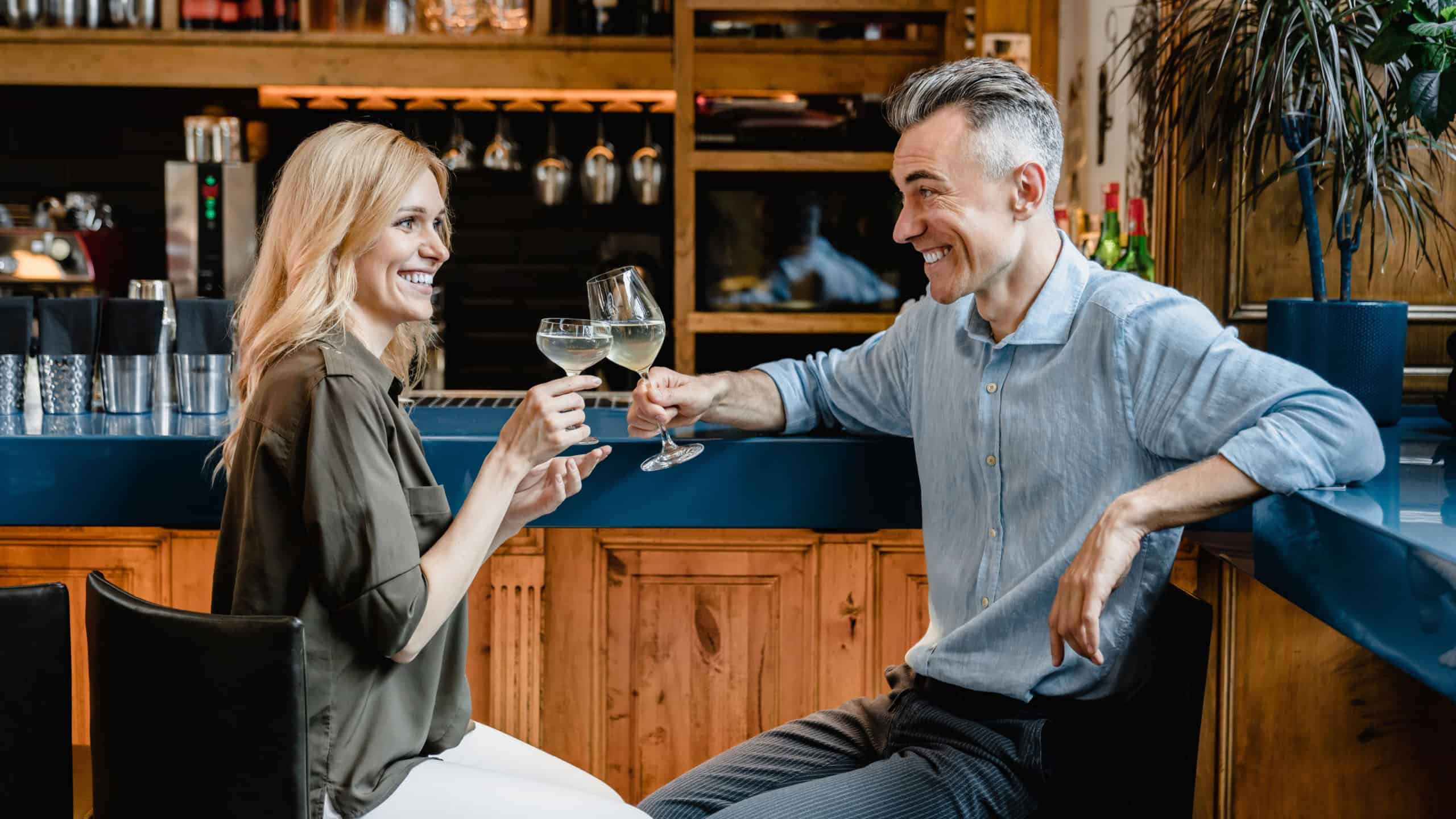 Love and relationship. Happy middle-aged couple drinking sparkling wine cocktails together on a romantic date toasting relaxing at the bar counter in cafe restaurant together.