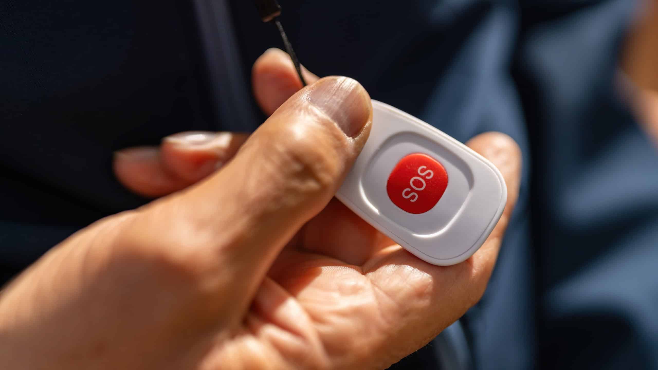 old hand holding an SOS button, highlighting its use for emergencies with focus on the red button