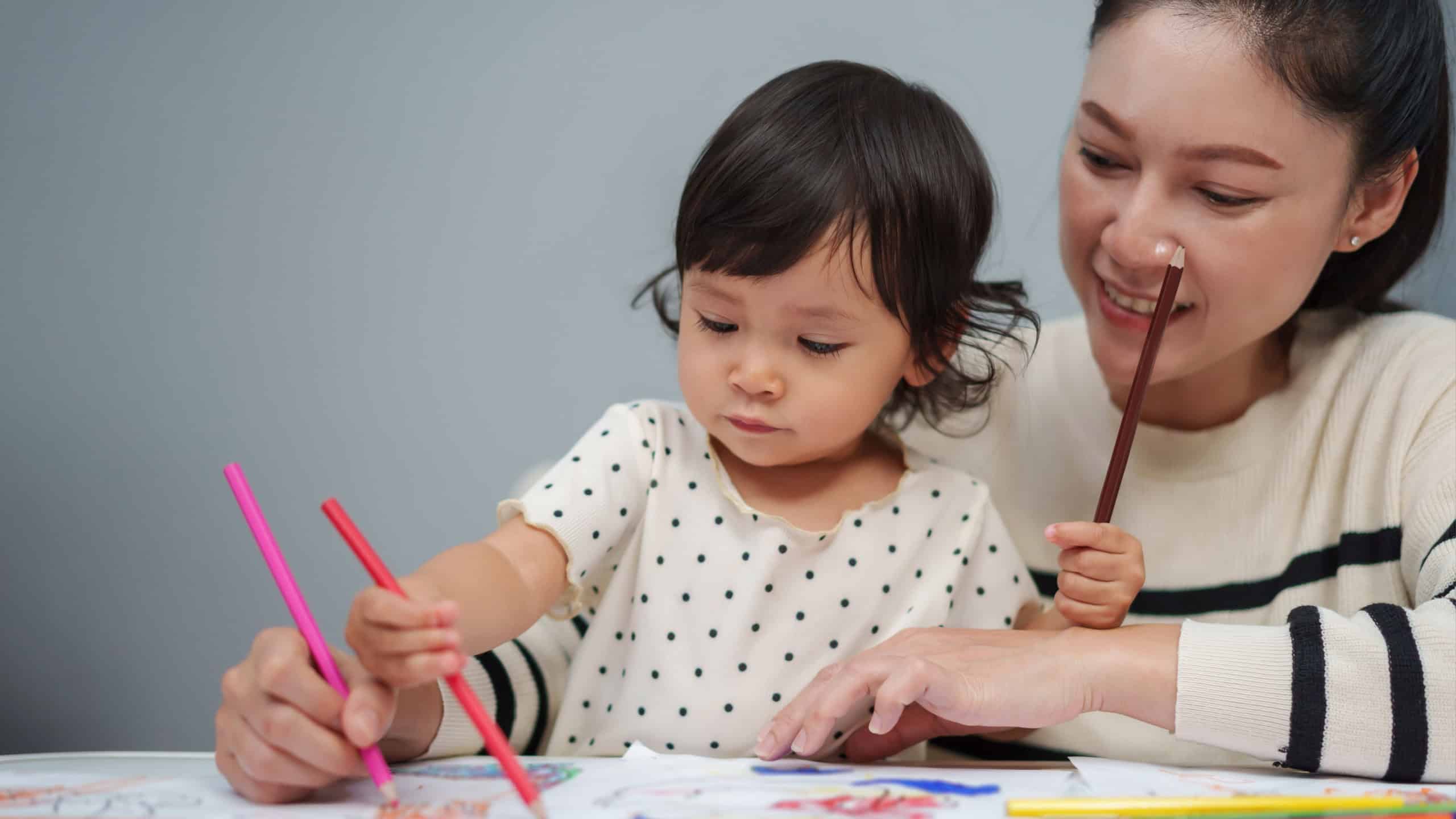 Toddler baby training to drawing with colored pencil with mother helping on the table