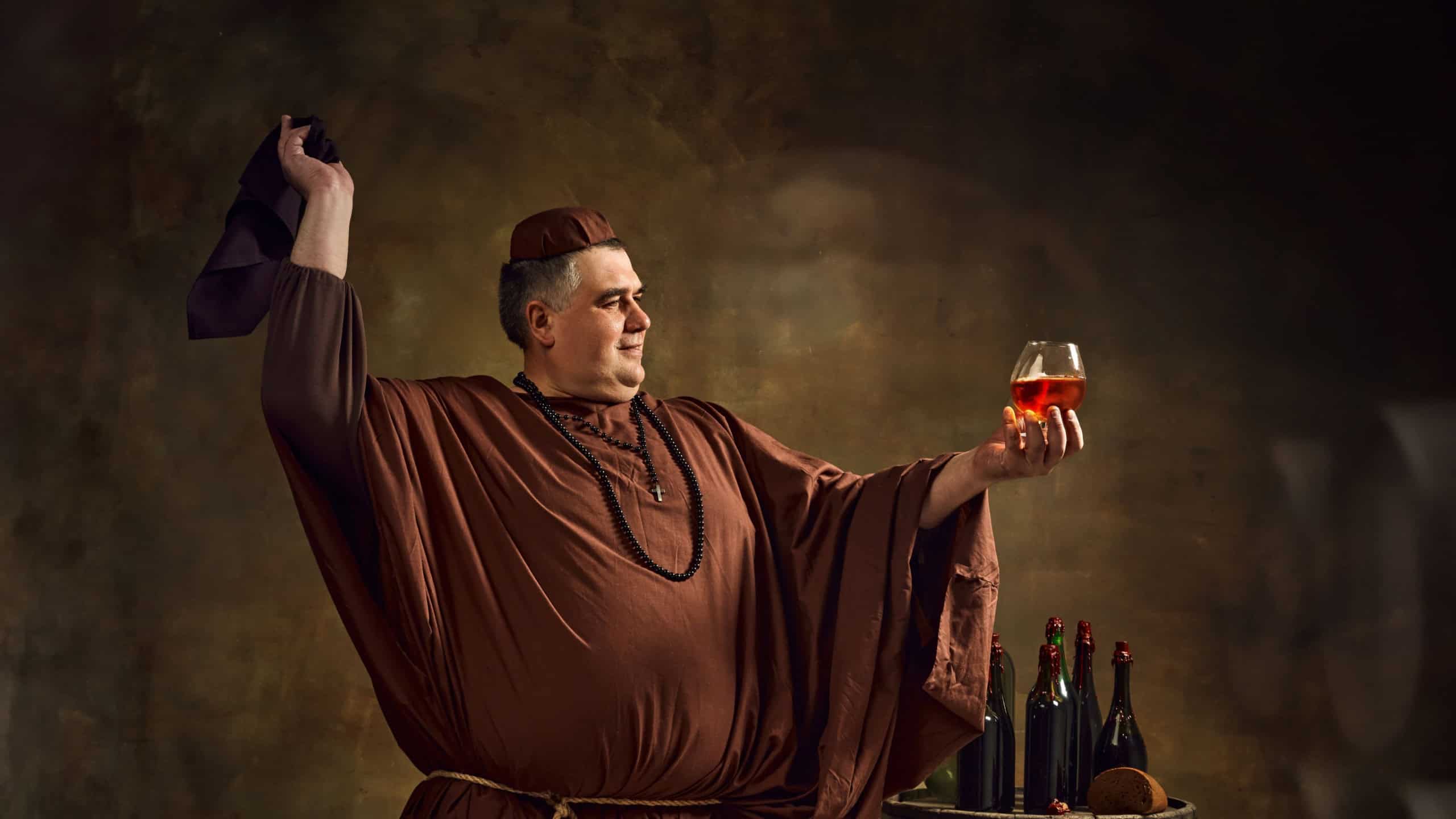 Medieval monk joyfully raising glass of ale, cognac or beer, showing rich tradition and celebration of Oktoberfest in monastic setting. Concept of comparison of eras, history, brewery, traditions