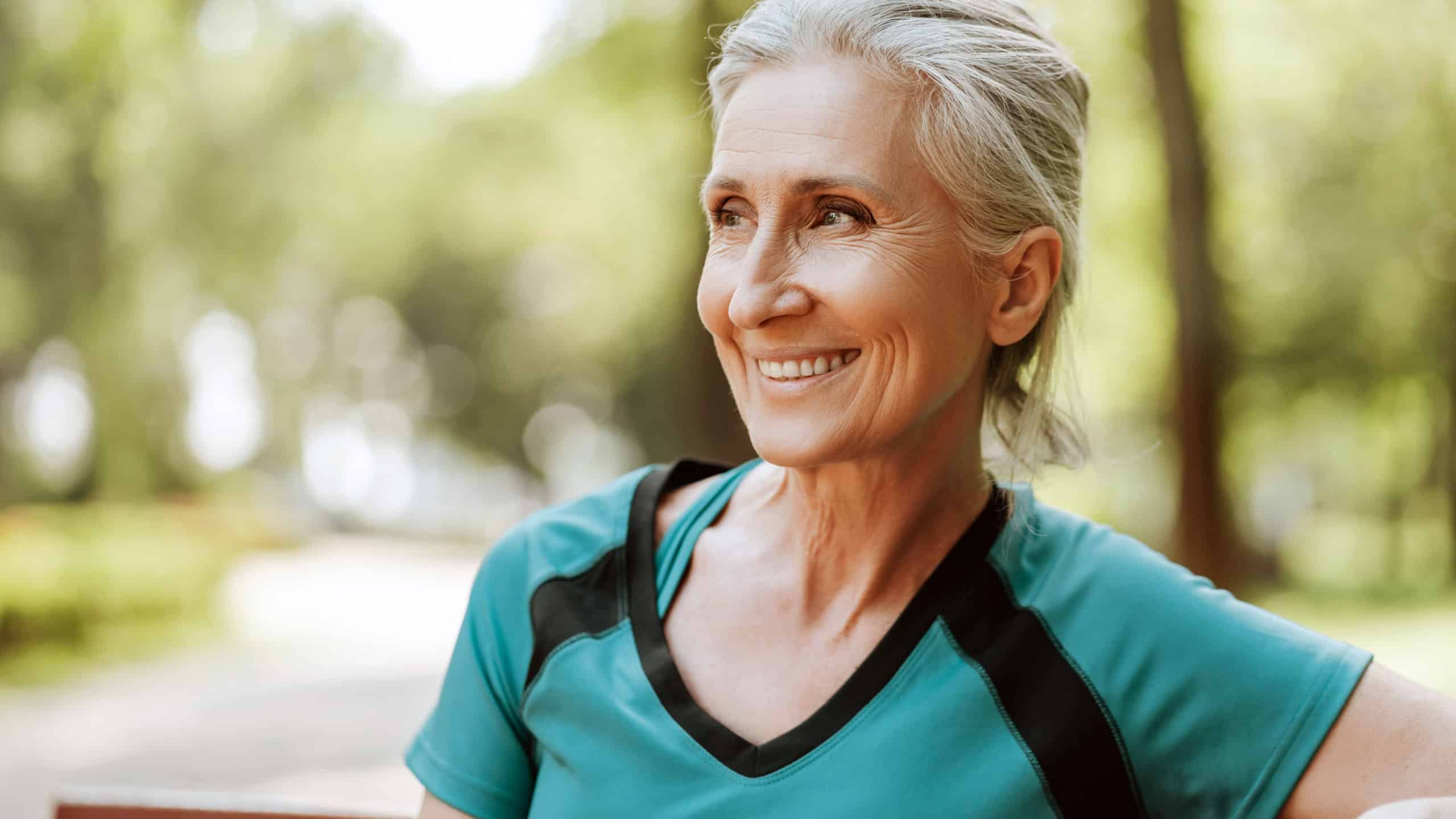 Senior woman smiling relaxing after exercising outdoors in park, looking away, fashion model posing, copy space. Natural beauty concept