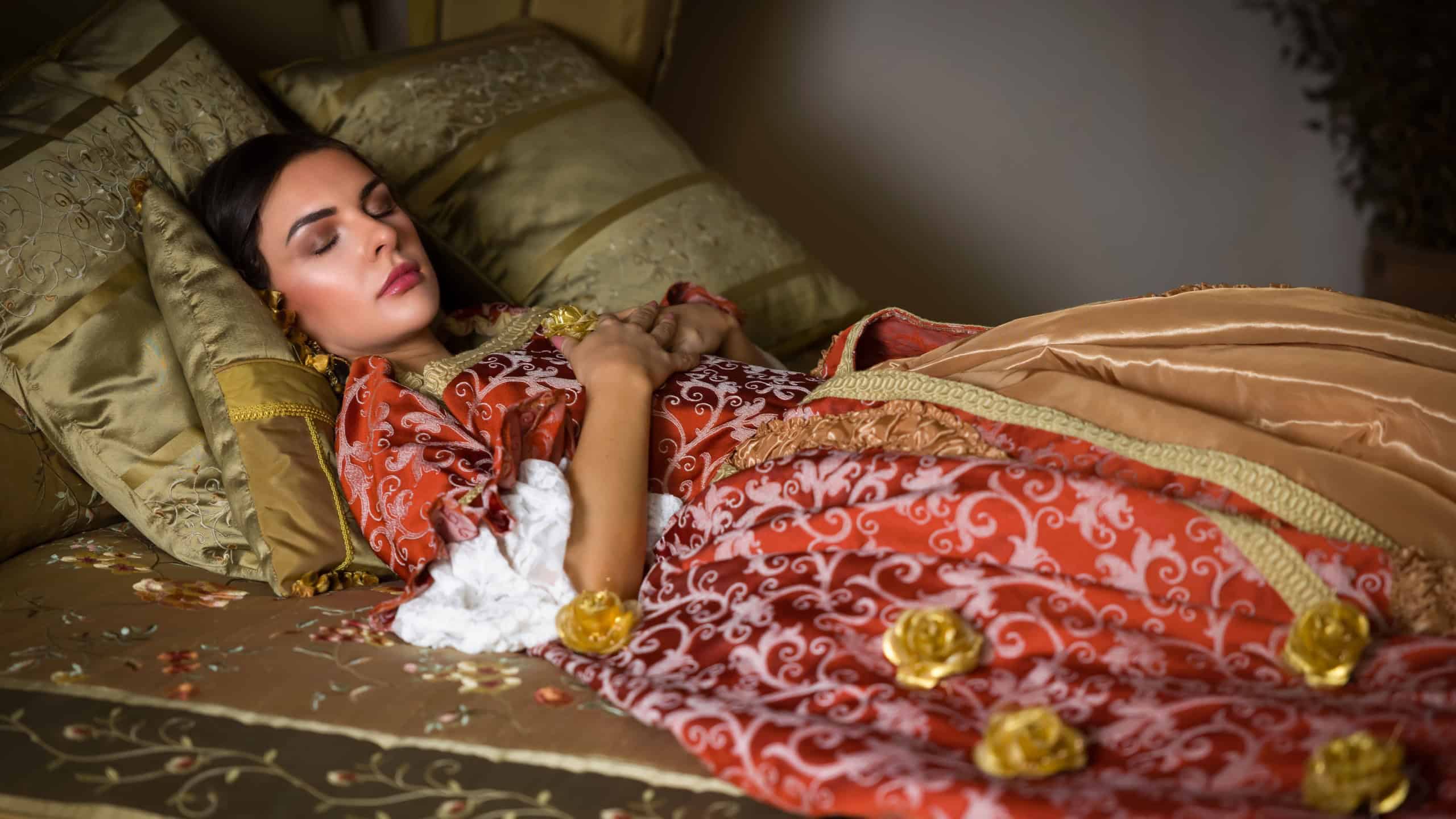 Golden medieval bedroom with beautiful canopy bed. A lady in renaissance dress lying on it in cinderella style.