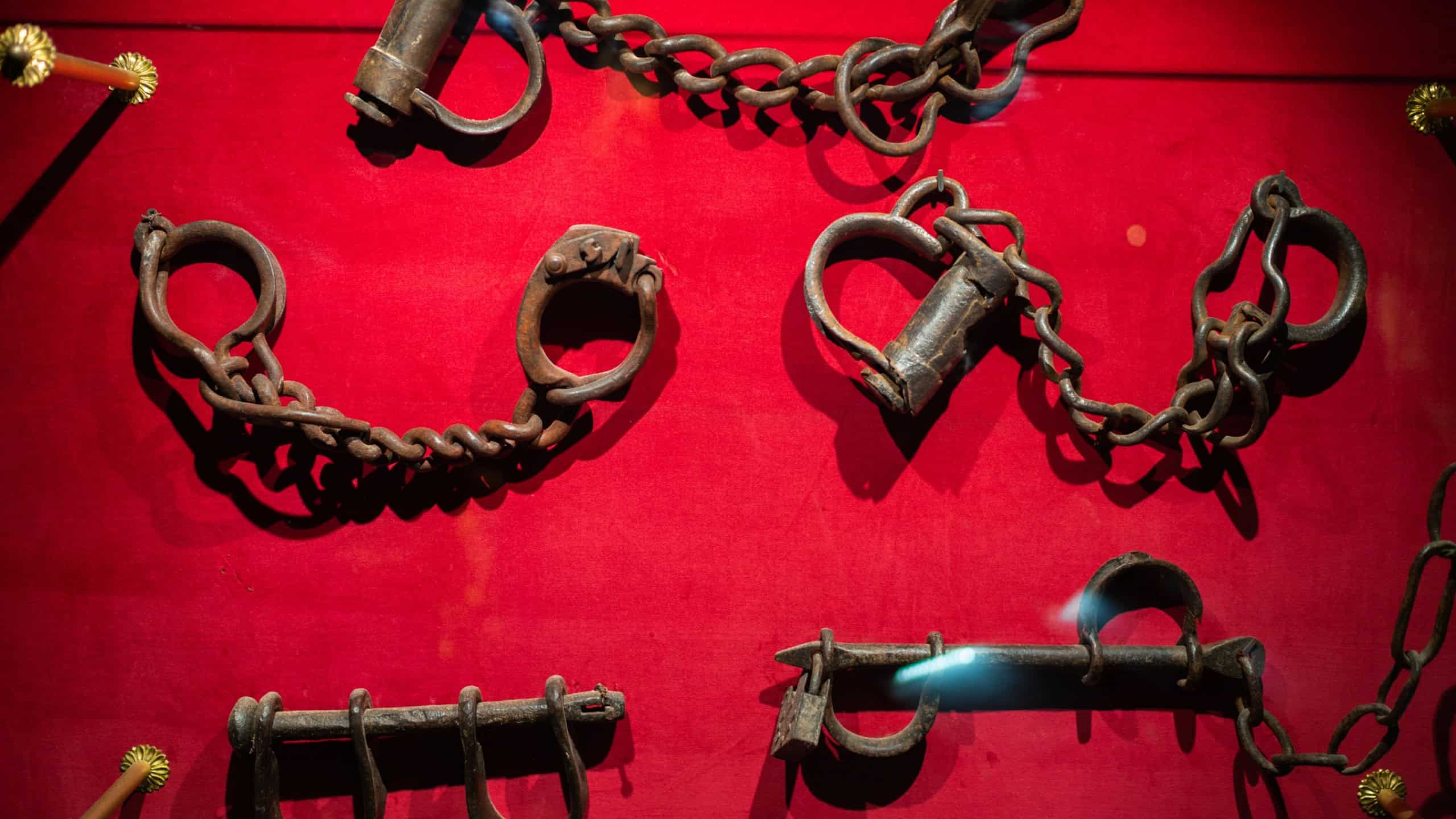 Collection of iron shackles and chains displayed on red background in medieval torture museum highlighting historical restraints