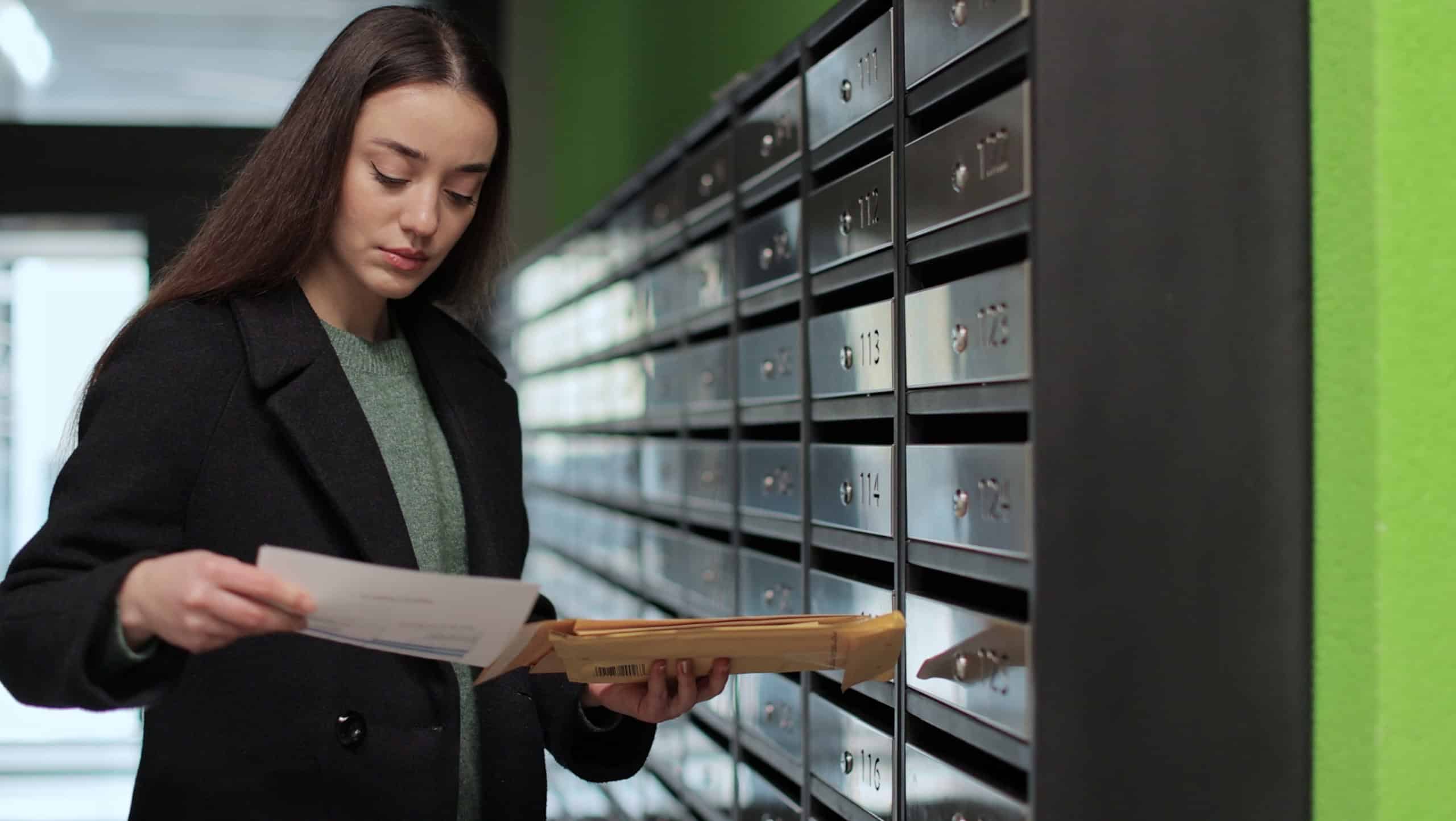 Woman is opening her mailbox inside a cluster of mailboxes for her apartment. Payment notification letter. Mail shipping concept.