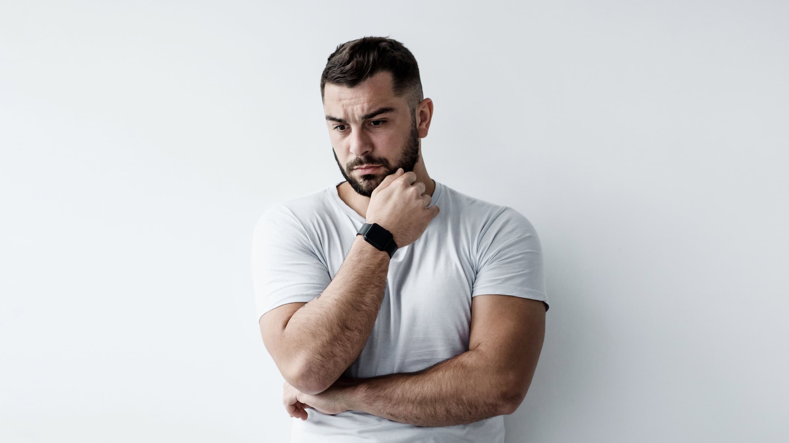 Think, solve problem, negative human emotions, stress and depression. Sad unhappy pensive young european handsome man presses hand to chin and ponders on white wall background, empty space, mockup