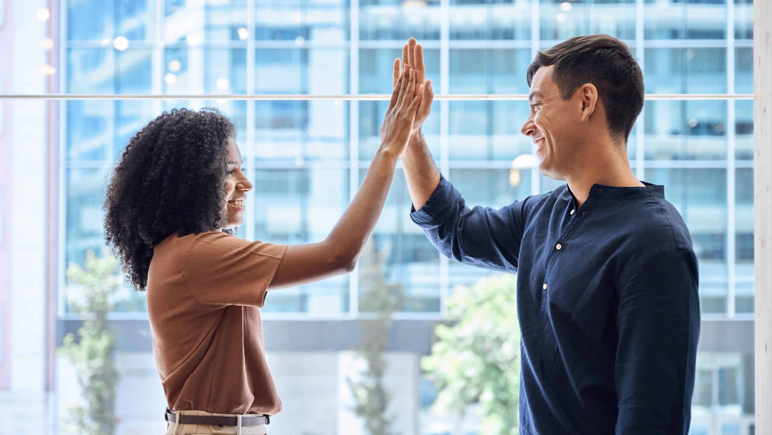 Happy diverse young team business people, two colleagues man and woman employees giving high five standing in office as concept of corporate success, leadership in teamwork, professional achievement.