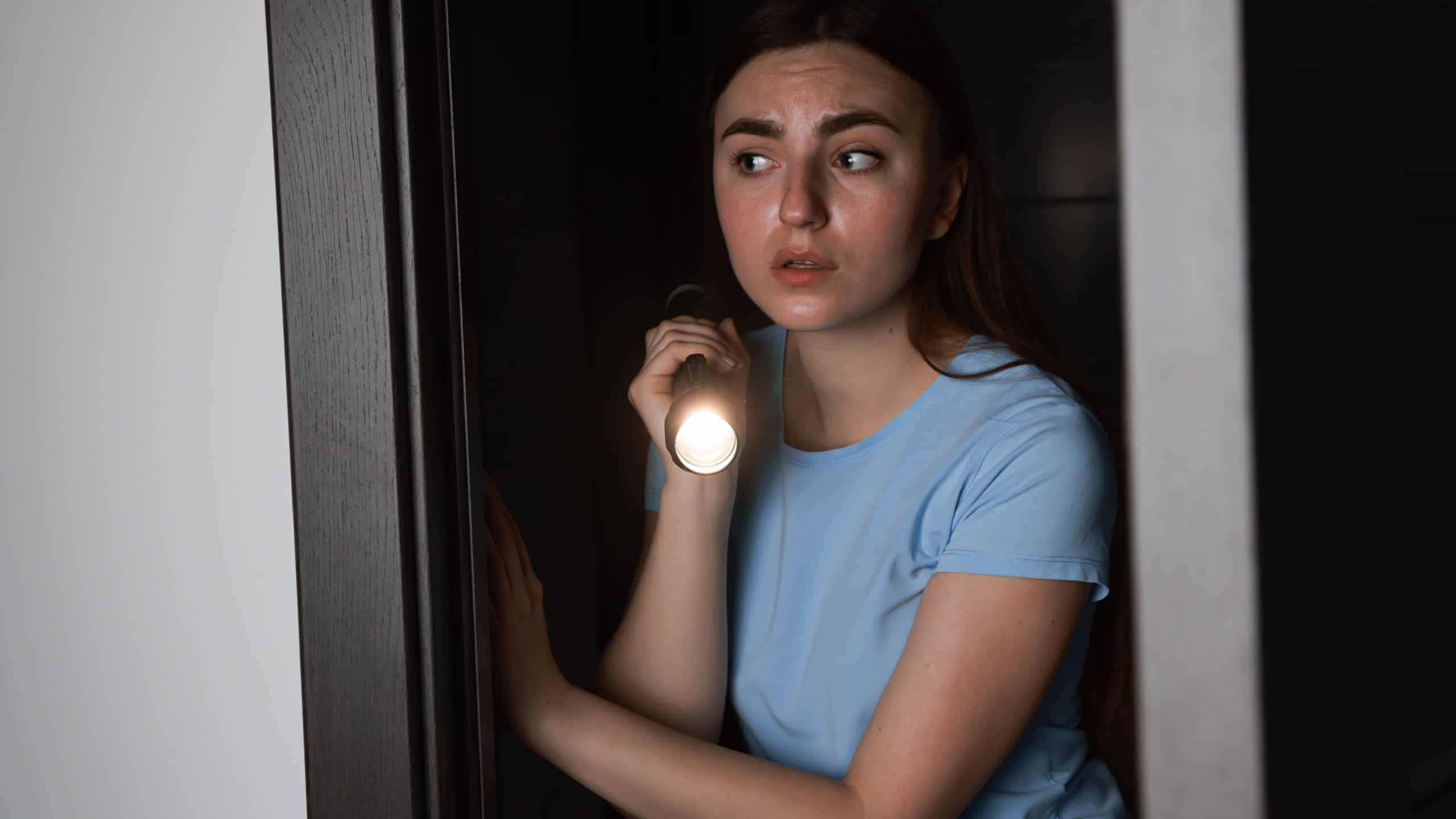 Fear of darkness. Scared young woman with flashlight indoors at night