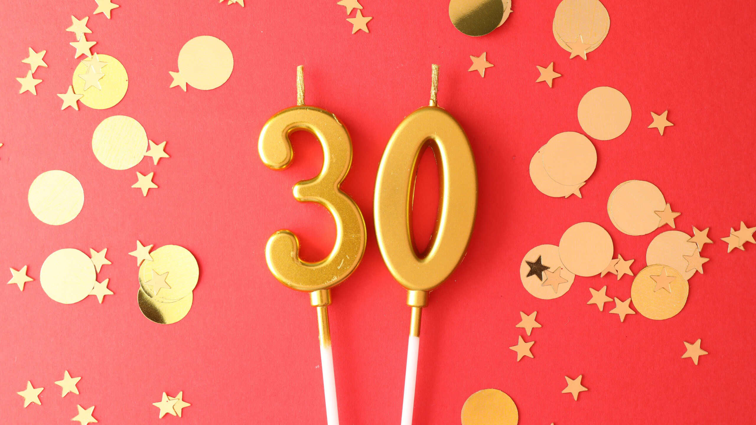 30th birthday. Number shaped candles and confetti on red background, flat lay
