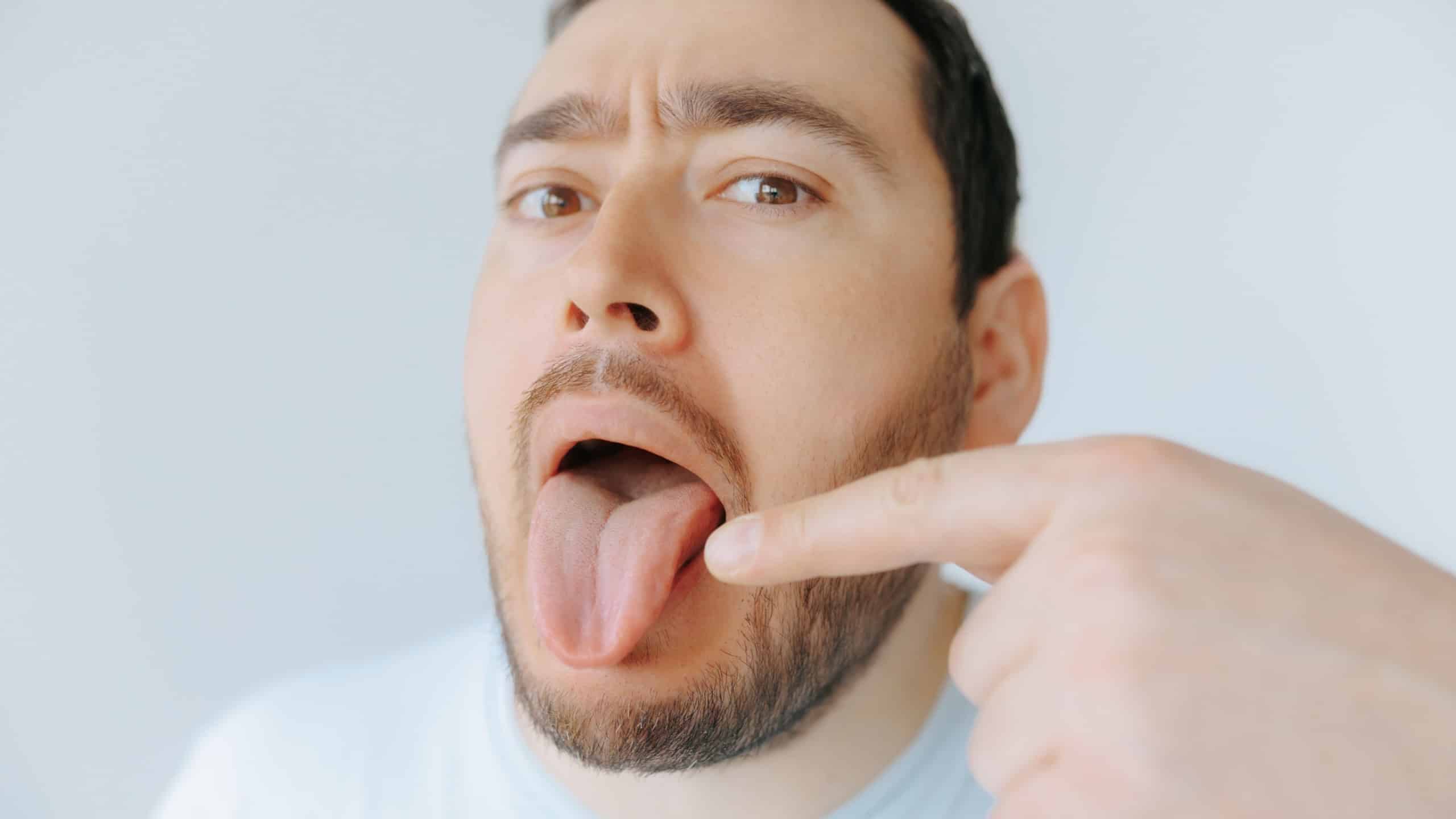 A man indoors is playfully sticking out his tongue while pointing at it with a finger. He appears to be having fun and enjoying a lighthearted moment.
