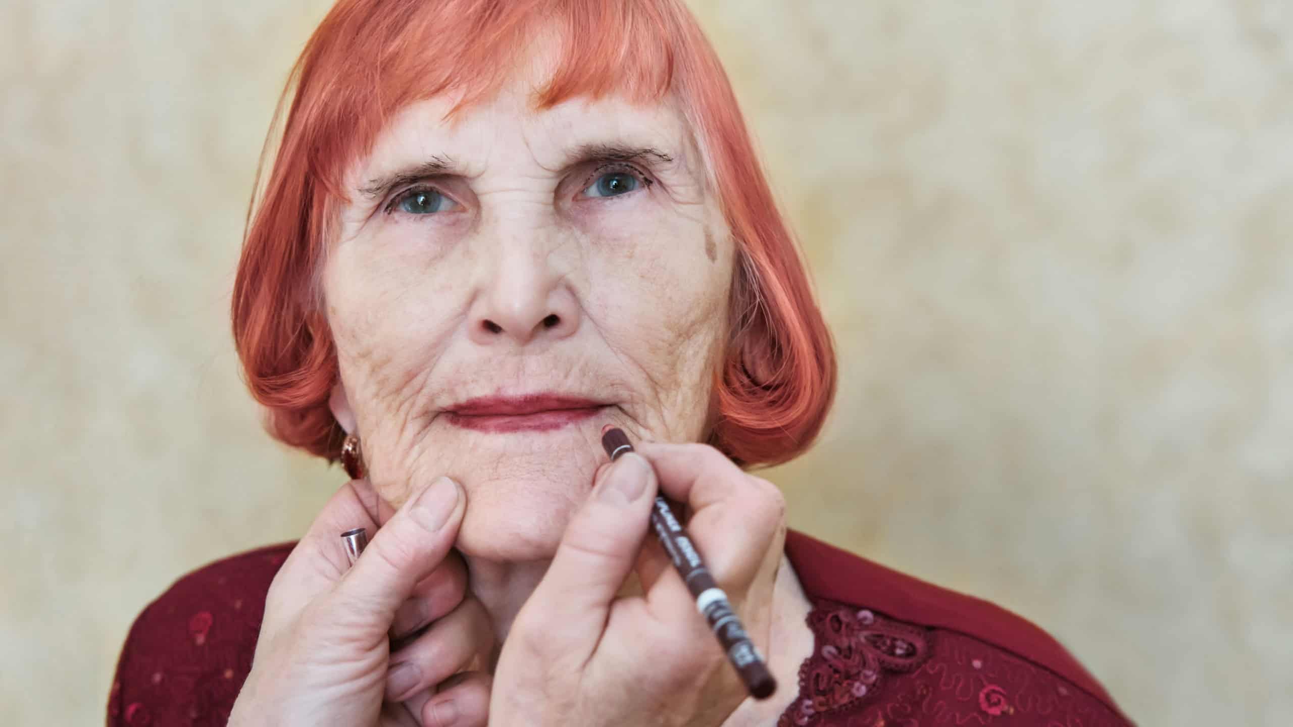 Elderly caucasian female receives makeup application by skilled hands